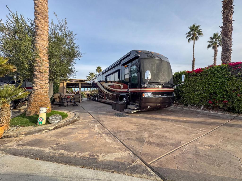 Perched on the coveted 'The Hill' at Outdoor Resort Indio, this expansive luxury RV lot offers one of the most stunning and wide-open views in the entire resort. Enjoy unobstructed panoramic vistas of the Chocolate Mountains, which transform beautifully as the sun sets, along with cascading waterfalls, three tranquil ponds, a charming bridge, and the lush golf course--all perfectly framed by an extra-wide opening in the elegant L-shaped Alumawood pergola. Designed for both privacy and comfort, the lot features a full-height privacy wall, a full rear electric sunshade, and ample accent lighting to create a serene ambiance day and night. Three ceiling fans and four heaters ensure comfort, while decorative pots and stylish bar stools add a touch of elegance to the outdoor living space.The spacious outdoor kitchen is an entertainer's dream, complete with a large island and bar, room for a full-size fridge, BBQ, and tiled cabinets for convenient storage. Hot water is readily available, making meal preparation effortless, while the thoughtfully designed layout provides both mid-lot and original post hookups for added convenience. Whether you're enjoying a peaceful morning coffee while watching the ducks on the ponds or hosting an evening gathering under the pergola's rubber-coated tarp roof with entertainment lighting, this lot offers the ultimate blend of luxury, comfort, and resort-style living. Come see the amazing view for yourself!‍Outdoor Resort Indio is a Class A only RV resort in Indio, CA.
