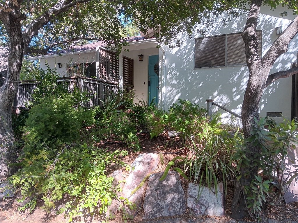 Incredibly charming home in the desirable Girard Tract of Woodland Hills, south of Ventura Blvd. Situated on a rare street-to-street corner lot, this private retreat is surrounded by mature trees with peek-a-boo views. Enjoy outdoor living on the wraparound deck and patio. Inside, a spacious living room features wood beam ceiling, a fireplace, and large plank wood floors. The updated kitchen offers ample storage, frosted glass door to outside, stainless steel appliances, and a large stainless sink. The primary suite includes a ceiling fan and en-suite bath with built-in storage and tile flooring. The second bedroom has a large built-in bookcase and opens to a private patio. Second full bath includes a stall shower. Both baths have custom vanities. Bonus room is previous carport/attached garage now studio/office (unpermitted) with vaulted ceiling, slider, and separate entrance—ideal for home office or gym. Additional features include a reverse osmosis water system, newer heat pump HVAC with Nest thermostat, tankless water heater, and DWP Flume leak detection system. Recently painted inside and out. A truly special property in a prime south-of-the-Boulevard neighborhood!