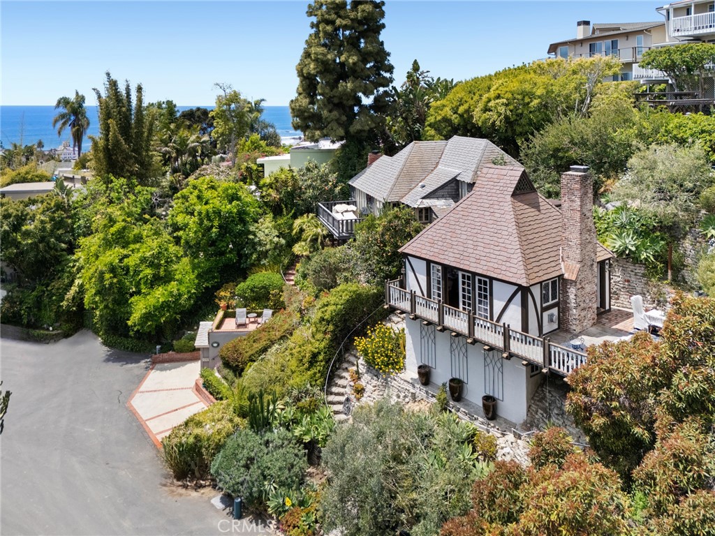 Located in the heart of Laguna Beach’s sought-after Village neighborhood, just moments from world-class beaches, galleries, restaurants, and boutiques, this Mills Act-approved home offers a unique blend of historic character, modern comfort, and valuable property tax savings. This one-bedroom, one-bath residence is truly one of a kind. Approximately 606 square feet and set on a wide frontage lot, the home features high ceilings, abundant natural light, and an open layout that flows seamlessly to outdoor decks and private patios. Lush gardens surround the property and create a welcoming setting in this cul-de-sac location. An upper garden terrace offers ocean and sunset views, enhancing the coastal lifestyle experience. An open floor plan highlights the main level, ideal for relaxing or entertaining in the living room with vaulted, open-beam ceilings, a brick wood-burning fireplace, and French doors that lead to a view deck framed by abundant greenery and the ocean. The kitchen connects to a rear deck and outdoor entertaining area, continuing the superb indoor-outdoor flow. The upper-level loft bedroom features stained glass windows, warm natural tones, and views of the ocean and gardens below. Each space in the home is designed to enhance comfort while preserving original architectural details. Located on Virginia Park Drive—a tree-lined, one-way street that loops around a landscaped median—this residence enjoys a serene, walkable setting that is truly unique in Laguna Village. This home presents a rare opportunity to own a distinctive property in one of California’s most desirable coastal communities, offering both charm and convenience in equal measure.