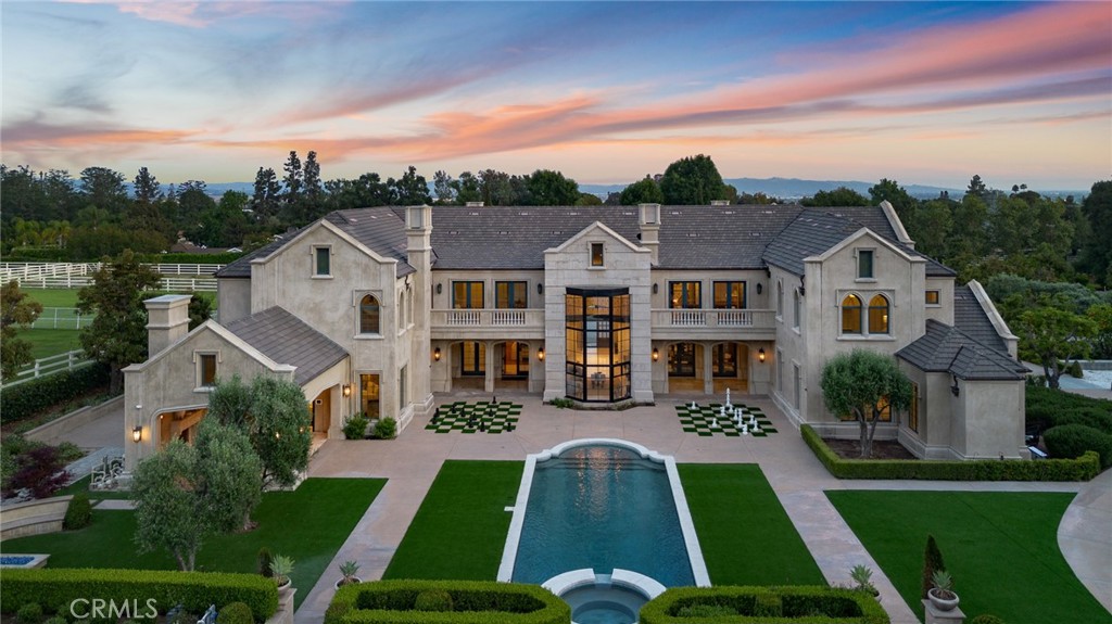 Just Reduced! Set behind private wrought-iron gates in the prestigious guard-gated enclave of Bradbury Estates, 18 Dovetail Lane is a masterfully designed English Tudor mansion that blends timeless architecture with modern luxury across an expansive 2.52-acre lot. With 10 bedrooms and 13 bathrooms, including a private 3-bed, 4-bath guest house, this estate is the ultimate in refined living.
The main residence offers 7 bedrooms and 9 bathrooms, showcasing soaring cathedral ceilings, gothic arches, fleur-de-lis detailing, and intricate woodwork. A soft neutral palette accented by antiqued metallics and natural finishes evokes both warmth and grandeur. Custom highlights include a gilded coffered library, gourmet kitchen with artisan cabinetry, secondary wok kitchen, private home theater, and dedicated spa room for ultimate relaxation.
Resort-style grounds are equally impressive, featuring a full-size basketball court, life-sized chess garden, sparkling pool and spa, and elegant formal landscaping designed for entertaining and peaceful retreat.
With its blend of European elegance and California luxury, this stately residence is a rare offering in one of Southern California’s most exclusive communities.