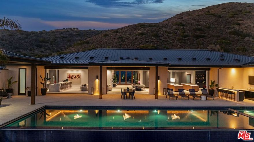 A palatial single-story estate influenced by the Four Seasons Hualalai brings resort-style living to Malibu. Set on two acres and designed by Doug Burdge, the compound features tennis/basketball court with pickleball, pool pavilion, gardens, two double garages, and the recently completed expansion of the flat backyard, which is on par with a sports pitch. Just a 20 minute drive from Camarillo Airport, the estate is one of 17 properties located in the exclusive 80-acre MariSol Malibu community. A Certified net zero carbon home that is 100% electric, featuring Tesla Powerwalls, solar panels, EV charging and endless eco-friendly features for a reduced carbon footprint. The main house is connected to the guest house via an interior glass bridge that is surrounded by lush tropical plants and ocean views. As you walk up the lanai steps and approach the grand front door entry you are welcomed with breathtaking ocean views stretching across the horizon. A perfect home for entertaining, the main kitchen is appointed with Miele and Gaggenau appliances, including three ovens, a built-in espresso machine and a reverse-osmosis water filtration system. Keep things clean up front with the secondary chef's prep kitchen, and enjoy the bar area with its four Gaggenau wine closets, beer tap and seating for six. The nearly 2,000 sq ft primary suite has whitewater views and sounds of the ocean waves. The suite includes a shou sugi ban water vapor fireplace, accoya wood ceiling, motorized doors and drapes, a large Poliform walk-in closet, a dual Porcelain-clad shower, and a rain-shower bathtub overlooking the ocean. This estate is a paradise for wellness seekers and includes a gym, steam room, Redwood sauna, water filtration system and a hospital-grade Merv 13 ventilation system. A verdant setting that's made to feel tropical, the exterior grounds include edible passionfruit, hibiscus and an organic fruit orchard and vegetable/herb garden. Offered fully furnished and decorated with art, the home is truly move-in-ready. Quick access to County Line surf break & beach, great seafood Neptune's Net Restaurant, and some of the best hiking trails in the Santa Monica Mountains.
