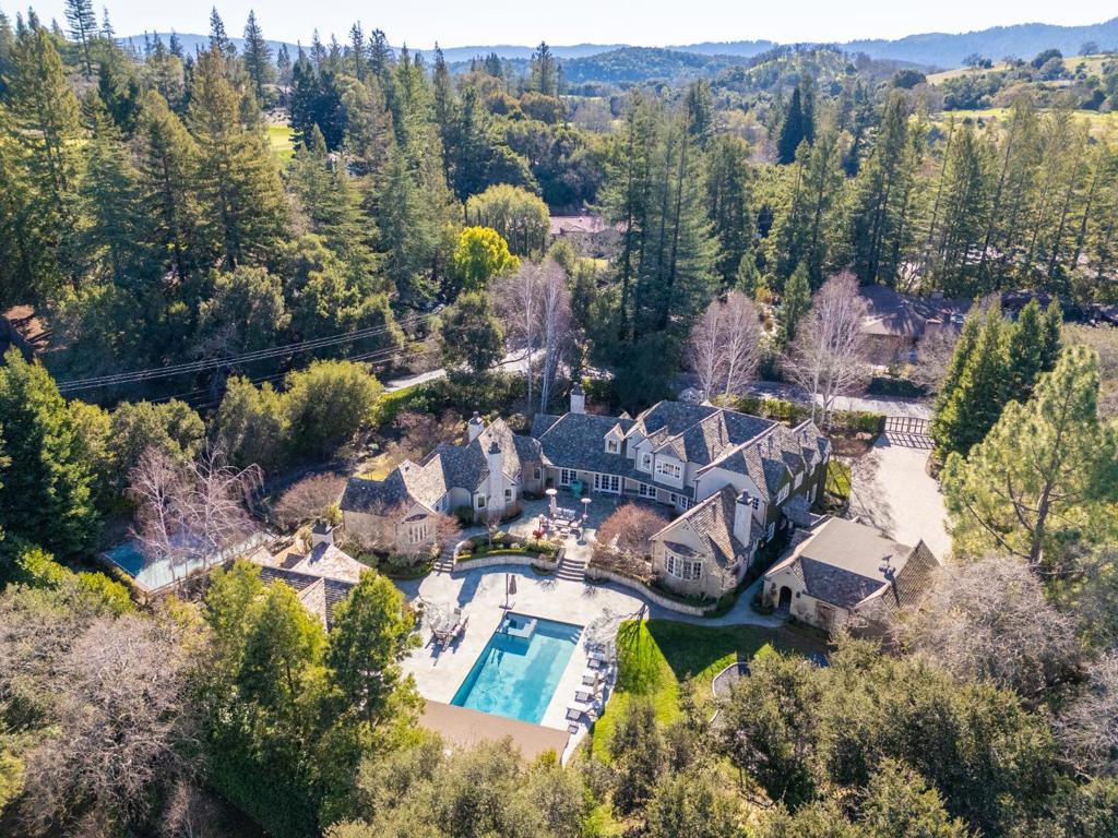 Located in Atherton, near Sharon Heights Golf and Country Club, this stunning modern Tudor-style estate rests on a gated, flat, park-like corner lot spanning over one acre. A paver driveway leads to the timeless stone and stucco residence, featuring a steeply pitched slate roof, ivy-covered walls, and exquisite landscaping. Inside, the grand foyer is bathed in natural light, with vaulted ceilings and French doors opening to the backyard terrace. The formal living and dining rooms, chef's kitchen with quartzite countertops and high-end appliances, and a family room with exposed trusses and crystal chandeliers offer elegance and functionality. The primary suite includes a fireplace, a luxurious spa-like bathroom, and French doors to the terrace. Three en-suite bedrooms, two lounges, and two laundry rooms complete the upper level. Outside, enjoy a saltwater pool, spa, heated cabana with a fireplace, outdoor kitchen, sports court, and a playhouse. The 1,134-square-foot pool house features vaulted ceilings, a full kitchen, two en-suite bedrooms, and a private entrance. With a three-car garage, wine cellar, walking paths, and proximity to premier shopping, schools, and the 280 Freeway, this estate offers unparalleled luxury and convenience, blending classic charm with modern living.