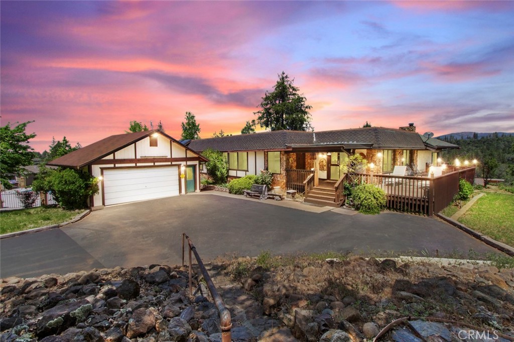 Welcome to your own Tyrolean-style retreat in the Sierra foothills - a home rich in charm, history, and character. Built in the late 1970s by the Cathrein family, this was the first home in what became a one-of-a-kind 55+ community. Inspired by the Austrian-German Tyrol region, it features custom architecture, a triple-wide manufactured layout on a permanent foundation, a stick-built great room addition, and a castle-style basement wine cellar with split door and stone surround.
Nestled on an elevated lot surrounded by mature oaks and evergreens, the property feels like a private park. The wraparound paved driveway offers extra parking and space for RVs, boats, or gatherings. A large front deck provides sweeping Sierra views and a quiet space to relax among visiting deer and wild turkeys.
Step inside through a carved wooden front door into a foyer wrapped in stained pine. Vaulted ceilings and exposed beams define the spacious living room, dining area, and family room with built-in wet bar and wall of windows. The kitchen is outfitted with granite countertops, stainless undermount sink, handsome cabinetry, matching appliances, and lots of storage. French doors open to a dramatic library featuring a floor-to-ceiling tiled fireplace, built-in oak shelving, and private access to the side deck.
The oversized primary suite includes vaulted ceilings, dual windows, a luxurious en-suite with soaking tub, walk-in shower, dual vanity, and makeup station. A spacious second bedroom offers a bay window and scenic views, while the hallway bath features a tub/shower combo and upgraded oak vanity. The indoor laundry room has built-in storage and its own exterior door to the deck.
Additional amenities include an oversized detached 2-car garage with workshop potential, a charming shed perfect as a detached office, and immediate access to the community’s clubhouse, pool, and raised gazebo. Community utilities include private water and sewer systems. A one-of-a-kind home in a legacy neighborhood. Welcome Home!!!