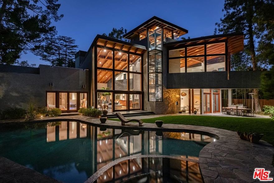 Designed by architect David Hertz, internationally recognized as a pioneer in sustainable architecture, this home is one of his most notable achievements. This gated property was designed/built to take advantage of its beautiful, wooded setting. The homes unique layout emanates from a large curved wall that makes a single arc from the front to the rear of the entire property. The richness in detail is beautifully realized throughout the entire open/airy floor plan in structurally unique ways. Nat light/wood, beamed ceilings/built-in cabinetry/wood and stone flooring. The interior spaces, specifically the voluminous living area and the exceptionally large, principal BR ste, feat. high roof planes which dramatically slope upwards towards the backyard realizing stunning double-height views. Four soaring sculptured fireplaces anchor the many living areas. Wet bar. Temp-controlled wine rm. Well-equipped gourmet cooks kitchen. Open den. The indoor-outdoor flow is seamless via big sliding glass panels to a private, expansive backyard w/ stunning views of the Stone Cyn reservoirs/hills/cyns w/ the city lights of LA as a backdrop. The Zen-like pool/spa are framed in natural stone/grass, creating a tranquil setting. Overlooking the panoramic vista is a sitting area w/ fire bowl. 3-car garage. Timeless architecture. A one-of-a-kind property w/ smart technology.