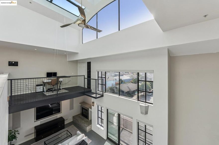 Chic and sophisticated top-floor, end-unit loft offering an open, light-filled living experience with multiple skylights and dramatic floor-to-ceiling windows capturing downtown Oakland views. With approximately 1,613 square feet, the expansive main level features concrete floors, a generous kitchen with breakfast bar, gas fireplace, contemporary lighting, and an open living and dining environment ideal for both everyday living and entertaining.  The mezzanine level overlooks the living area and provides a large, flexible bedroom space with potential to be configured into two private rooms. A catwalk workspace offers an ideal office or creative area. Additional storage is plentiful, including a spacious, stand-up attic accessed by pull-down ladder. The primary closet has been enhanced with a custom organization system for optimal storage and function.  The home is wired for integrated smart home functionality for lighting, climate, and audio/visual components. Secure garage parking with additional storage included. A rare blend of volume, light, storage, and flexible living space in a true urban loft setting.