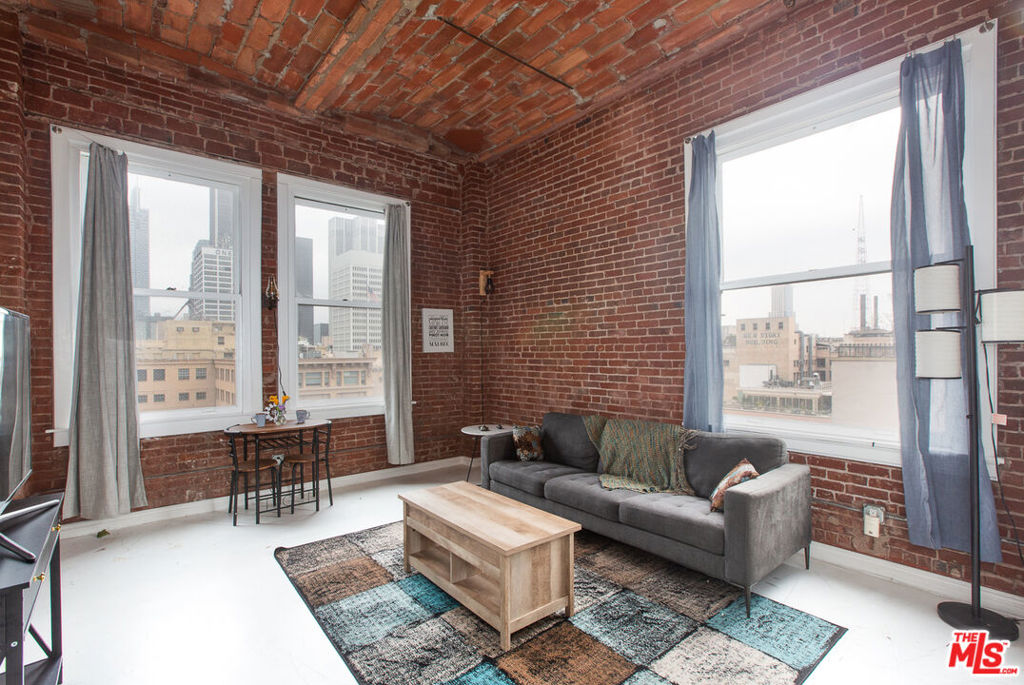Welcome to your own private escape in the sky at the historic Bartlett Building in Downtown Los Angeles. Unit #1301 is a higher-floor, corner one-bedroom loft offering sweeping views that stretch to the west over the dazzling Downtown skyline and north toward the iconic Los Angeles City Hall. If you're looking for a home that blends historic character, architectural charm, and modern updates, this loft delivers it all. Step inside and you're immediately greeted with soaring ceilings of approximately 12 feet, massive original industrial-style windows that flood the space with natural light, and details that speak to the building's 1911 Beaux-Arts origins. Exposed brick walls and polished concrete floors add to the authentic loft aesthetic, creating an atmosphere that feels both dramatic and welcoming. Unlike many open lofts in the city, this home features a true enclosed bedroom, giving you the privacy you want without compromising the expansive, airy feel of the space. The floor plan also naturally separates the bedroom area from the living and entertaining spaces, making the layout both functional and versatile. The updated galley-style kitchen is compact yet highly functional, outfitted with stainless steel appliances, a full-size refrigerator, plentiful cabinetry, and ample counter space for cooking or entertaining. The bathroom includes a larger soaking tub, modern tile, and updated fixtures, making it an inviting place to relax and unwind. To complete the package, a full-size washer and dryer are located in-unit, an invaluable convenience in the heart of Downtown.As a resident of the Bartlett, you'll enjoy an array of amenities that enhance both lifestyle and peace of mind. The building offers 24/7 front desk security, plentiful rentable storage space, a landscaped third-floor outdoor courtyard perfect for a quiet break, and a rooftop deck with jaw-dropping 360-degree views of the Downtown skyline and beyond. Whether it's sunrise yoga, sunset cocktails, or simply taking in the sparkling city lights, the rooftop offers one of the most impressive vantage points in all of DTLA. Another exceptional benefit of ownership at the Bartlett is the Mills Act designation. This coveted status provides significant annual property tax savings, which can add up to thousands of dollars per year, making this loft not only a stunning home but also a smart investment. Parking is not deeded with this unit; however, secure on-site parking is available for rent, and additional nearby options make commuting and car ownership easy if needed. Living at 215 W 7th St places you in the heart of the Historic Core, just steps from some of the city's most celebrated restaurants, bars, coffee shops, and cultural landmarks. Whether you're in the mood for fine dining, live music, a gallery opening, or just a quiet coffee around the corner, everything you could want is within a short walk. The neighborhood also offers convenient access to Metro stations and freeways, connecting you easily to the rest of Los Angeles. Unit #1301 at the Bartlett Building is more than just a loft, it's a lifestyle. With historic charm, modern updates, breathtaking city views, and access to all that Downtown has to offer, this property represents a rare opportunity to own a true piece of Los Angeles history while enjoying the best of contemporary urban living.