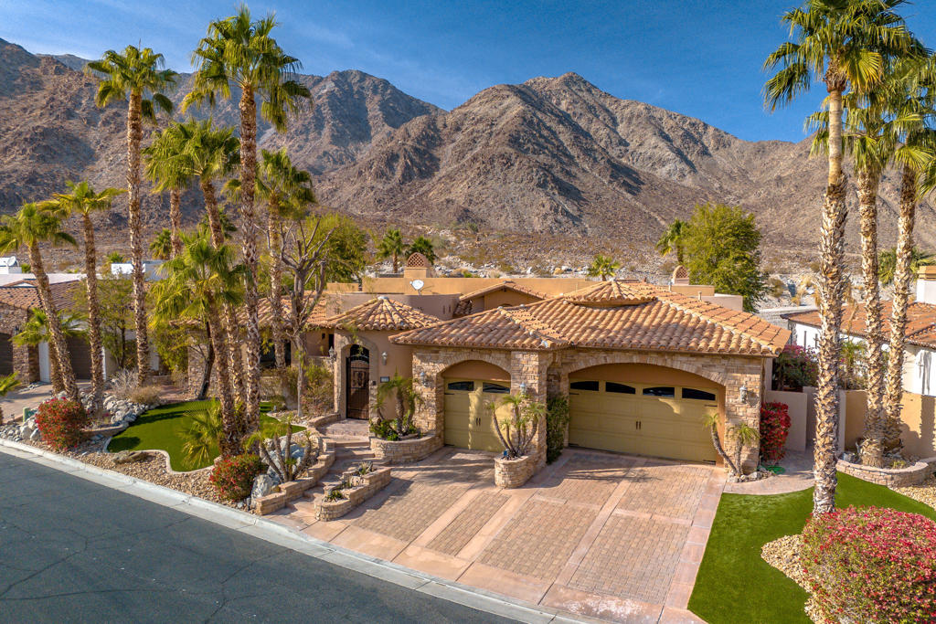 Mountainside escape! With over 4,286 square feet of living space including four bedrooms and three and a half bathrooms. This home features a spacious and inviting entryway that leads into a layout with vaulted ceilings, allowing for abundant natural light throughout the interior. The primary bedroom showcases a serene ambiance with scenic mountain views, and a spacious private retreat with fireplace. The kitchen boasts ample cabinetry and granite countertops, complementing the overall thoughtful design. Gourment kitchen with six burner stove and grill, a pot filler and mirrored back splash. Heading outside, the home's lush landscaping creates a tropical oasis, complete with an outdoor patio and outdoor bar area with mood lighting, ideal for entertaining or relaxation. The gated community adds an extra layer of security, while the spacious driveway provides ample parking with a three-car garage. Low HOA fees. The backyard blends the indoors and outdoors seamlessly. Ultimately, this home presents an ideal setting for those seeking a balance of comfort, style and connection to the surrounding natural beauty of the mountains. Close to Old Town La Quinta, La Quinta Resort and so much more.