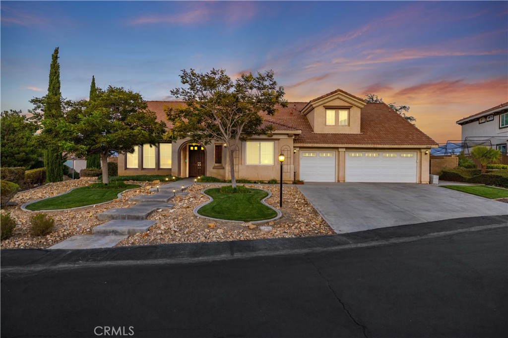 This gorgeous corner property, surrounded by tall trees, lush greenery, and beautiful views, is located on a cul-de-sac in the prestigious Renaissance gated community of West Palmdale. Offering 3,607 sq. ft. of elegant living space on nearly half an acre with RV access, this 2004-built home features two primary suites—one on each floor—making it ideal for multi-generational living or guest accommodations. The professionally landscaped front yard showcases a custom walkway and a three-car garage. Inside, a tile entry opens to a formal living and dining room with custom lighting and a built-in bar, perfect for entertaining. Just off the entry, a double-door flex room (office/library/den) provides a private and versatile space for work, study, or relaxation. The remodeled kitchen shines with upgraded granite countertops, subway tile backsplash, sleek white cabinetry, and brand-new stainless steel appliances. An island with seating, space for a dining table, and a glass door to the patio create the perfect gathering space. The adjoining family room features a cozy fireplace, built-in shelving, and abundant natural light. The oversized downstairs primary suite offers a professionally organized walk-in closet and sliders that open into a sunroom for year-round enjoyment. Its spa-style bathroom includes dual sinks, a vanity, soaking tub, and walk-in shower. Upstairs, a large loft serves as a second living area, alongside another spacious primary suite with a walk-in closet and full bath. Two additional generously sized bedrooms feature ample closet space, while built-in cabinetry with drawers throughout the home provides exceptional storage and functionality. A laundry room with sink and storage adds convenience. Outside, the backyard oasis offers a covered patio, custom pathway, lush lawn, mature trees, and block walls for privacy. This exceptional property combines comfort, flexibility, and luxury in one of Palmdale's most desirable communities.