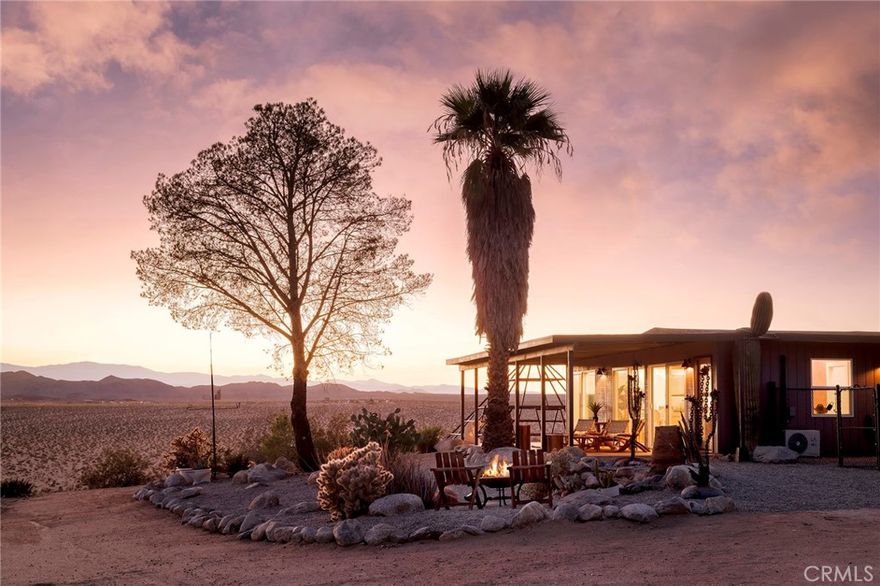 29 WEST PYRAMID HOUSE: Perched on the top of its own mountain, this striking 2-bedroom, 2-bathroom retreat delivers 360-degree views spanning Indian Cove in Joshua Tree National Park, Big Bear, and San Gregorio. Framed by dramatic imported boulders and pristine desert landscape, the property offers a rare blend of privacy, serenity, and natural beauty. At night, the dark skies transform into a stargazer’s dream, making this a true High Desert sanctuary.

The centerpiece of the landscape is a bold steel-frame pyramid, measuring 24' x 24' x 14', positioned at the mountain’s edge. This dramatic outdoor structure creates a visual anchor and an unforgettable backdrop for both day and night desert living.

Inside, the home is curated with Venetian plaster walls, lime wash finishes, and custom vertical plaster striping. The open floor plan is framed by expansive sliding glass doors and an 8-foot picture window, pulling the desert scenery directly into the living space. Spa-inspired bathrooms feature floating vanities, backlit mirrors, wood tile, and marble finishes, blending sophistication with soothing desert textures.

A shaded porch extends from the living room, offering a peaceful vantage point for sunrise coffee or evenings under the stars. Custom channel lighting in the living room mirrors the sharp lines of the pyramid, emphasizing the interplay of geometry and desert landscape. The large kitchen showcases brand-new counters, custom cabinetry, and generous storage — designed for both everyday use and stylish entertaining.

Centrally located at the edge of 29 Palms and Joshua Tree, this property is just minutes from both villages, with easy access to shops, restaurants, and Joshua Tree National Park. Blending bold design, natural elements, and complete privacy, this mountain-top retreat embodies modern desert living at its finest — the kind of home you’d expect to see in the pages of Architectural Digest.