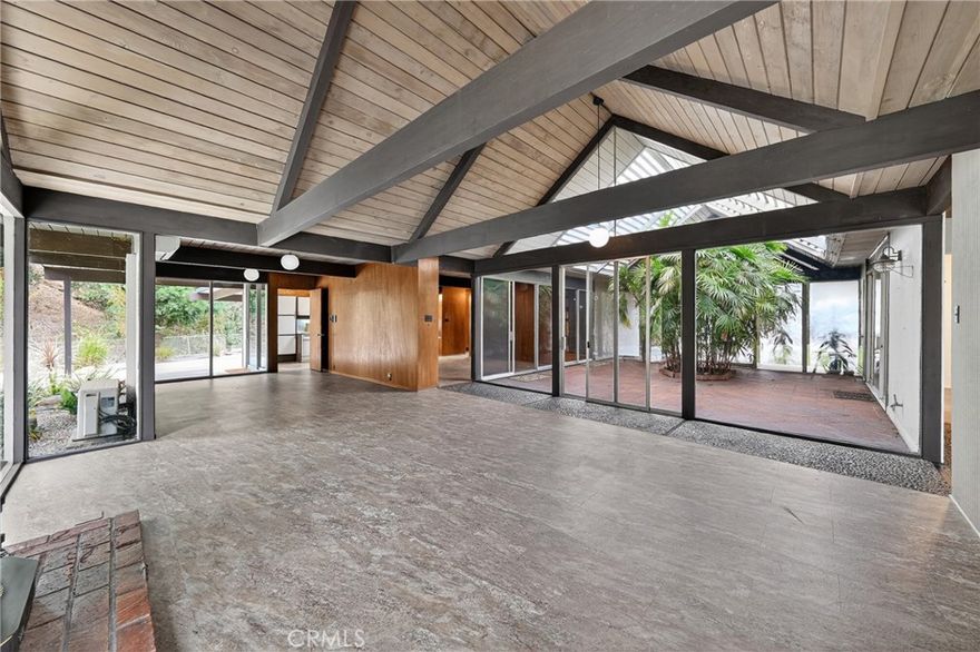 Step into iconic California living with this beautifully preserved mid-century modern home, thoughtfully designed by famed architects A. Quincy Jones and Frederick Emmons. This expansive five-bedroom residence celebrates light, space, and design with its signature open-beam ceilings, walls of glass, and seamless connection to nature. At the heart of the home lies a tranquil private atrium — an ideal setting for morning coffee, quiet reflection, or evening gatherings. The primary suite opens to a lush, park-like backyard that extends the living space outdoors, perfect for relaxation or entertaining under the California sky. Positioned at the end of a peaceful cul-de-sac on an oversized lot with no rear neighbor, the property offers a rare sense of privacy and retreat. Experience the timeless sophistication of mid-century modern living — where thoughtful architecture and natural beauty create a lifestyle that feels both refined and restorative.