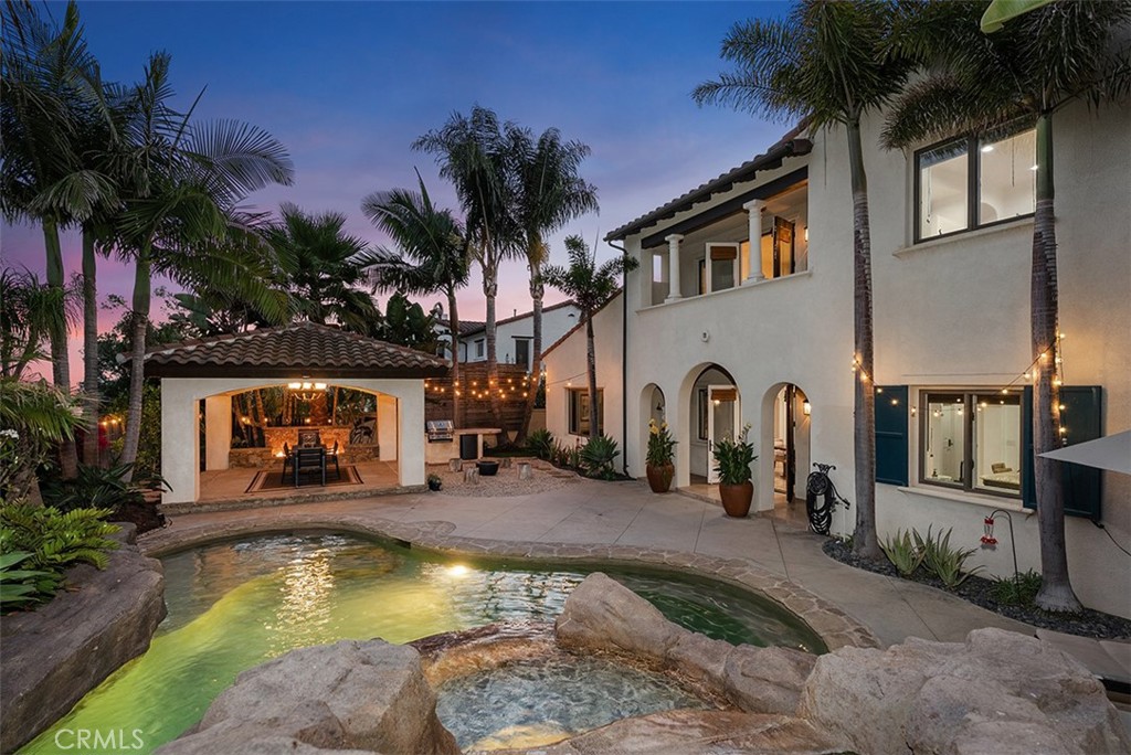 Every now and then, a residence comes along that truly delivers on the promise of having it all. Welcome to this San Clemente estate, poised behind the prestigious gates of Talega’s exclusive Careyes enclave, where panoramic golf course views, privacy, refined enhancements, and an expanded floorplan set the stage for an extraordinary lifestyle. The grounds recall a private resort, with graceful palms rising over a backyard centered on a lagoon-inspired saltwater pool with water slide, Baja entry, sculptural rockscapes, and spa. Ocean breezes accompany al fresco dining within a custom pavilion featuring a dramatic fire and water element, seamlessly integrated with a built-in BBQ and beverage refrigerator. Nearly 10,237 square feet, the homesite extends indoor-outdoor living with an elevated front patio and, beyond a privacy door, a generous lawn and fireplace lounge for evenings under the stars. Inside, luxury continues across approximately 4,689 square feet, offering five ensuite bedrooms and five-and-one-half baths, complemented by a detached casita off the entry courtyard—ideal for an office, gym, or retreat. A second-floor bonus room expands possibilities, easily adaptable to an additional bedroom if desired. The foyer, opening through French doors to the courtyard, flows into a formal dining room crowned by a barrel ceiling and a great room anchored by a sandstone fireplace with views to both courtyard and backyard. A breakfast room connects to the outdoors and to a chef’s kitchen designed with beauty and function, featuring granite countertops, stained-wood cabinetry, a butler’s pantry, walk-in storage, and a built-in refrigerator alongside a professional Thermador range with six burners, two ovens, and griddle. For added convenience, the downstairs suite includes a custom bath with direct pool access. Secondary bedrooms are generous—one distinguished by twin Juliet balconies and a versatile study niche. The primary suite, oriented to golf course and hillside views, is a sanctuary with cast sandstone fireplace, custom walk-in closet, dual vanities, and jetted chromotherapy tub. Upgrades include solar power, wood and travertine flooring, Walker Zanger limestone in baths, whole-house audio, and recirculating hot water. Even the three-car garage is finished with epoxy flooring and built-in storage. This is a home that pairs the intimacy of coastal living with the sophistication of architectural design—an address where every detail has been considered.