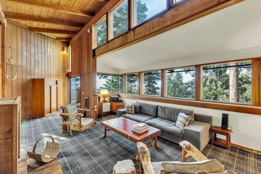 This architectural gem, designed by renowned architect Dennis McGuire as his first project in Idyllwild, CA, is a breathtaking masterpiece anchored and pinned to massive granite boulders, some of which grace the interior of the home. Clad in Simpson Redwood plywood with resawn redwood accents inside and out, the home seamlessly blends natural elements with modern design. Expansive views span from Mount Wilson-aligned with the summer solstice sunset-to Mount San Gorgonio and Black Mountain. The main level boasts a light-filled kitchen with tiled counters, a dining area, and a living room with soaring ceilings, a dramatic fireplace, and unparalleled vistas. The primary bedroom opens to a private deck for peaceful mountain moments. A lower-level guest room, featuring a cozy bay-like nook framed by glass, offers space for an office or serene retreat. Relax in the skylit shower, soak in the top-quality hot tub, or unwind on multi-level decks surrounded by nature. This rare visual jewel invites you to experience a harmonious balance of nature and design.