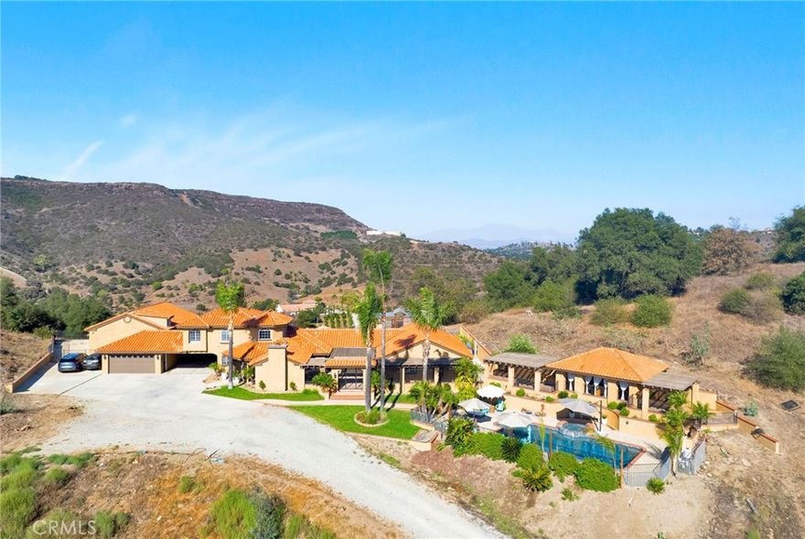 Welcome home to this stunning Mediterranean-inspired estate, set amidst the breathtaking views of Temecula Wine Country. Nestled on 8.63 peaceful acres of rolling land, this property offers the perfect balance of tranquility and luxury. The main home spans a generous 3,579 square feet and has recently undergone an extensive, high-end remodel. It features a beautifully appointed main-level primary suite, a junior suite, a guest bathroom, and a separate laundry room with ample storage. Upstairs, you’ll find an additional suite with two bedrooms, each with its own closet, and a shared full bathroom. The heart of the home is the chef’s kitchen, complete with top-of-the-line appliances, stunning "Knotty Alderwood" cabinetry, sleek granite countertops, and a cozy breakfast nook. The great room boasts a stately Venetian plaster-style fireplace, while the formal dining area offers the perfect setting for dinner parties. Step into the living room with a second fireplace, adding elegance to the living spaces. Throughout the home, you’ll enjoy beautiful engineered hardwood flooring, complemented by gorgeous tile and stone accents in the bathrooms. Multiple patios, including an expansive covered patio system, provide plenty of space for outdoor living. The outdoor cabana-style room with a mounted TV is perfect for entertaining, while the uncovered firepit patio overlooks your sparkling pool and spa—ideal for relaxing and unwinding. For extra versatility, an attached bonus room near the covered carport offers a great space for additional sleeping quarters, a gym, or a flexible room to suit your needs. The detached, two-story, 6-car garage is a true standout, featuring roll-up doors, a bonus/office space with a beautiful cabinet and sink, and an additional upstairs studio. The amazing backyard has panoramic views, multiple patios, planter boxes and pots around the backyard, along with a pickleball area and putting green. Additionally, there is a spacious chicken and small animal coop, plus 2 more small animal stalls on the lower level. With its stunning outdoor spaces, captivating views, and quality upgrades throughout, this property offers everything you could want in a home. There’s truly no place like it!