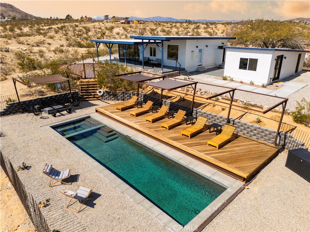 Welcome to Casa Azul, a modern desert retreat set on 2.5 private acres in the heart of Joshua Tree. Just 7 minutes from town and 20 minutes from the National Park, this thoughtfully renovated 3-bedroom, 3-bath home (2 bed main house/1 bed casita) blends contemporary design with the raw beauty of the desert landscape. The property was reimagined with entertaining and relaxation in mind, featuring a sparkling saltwater pool, in-ground spa, outdoor shower, propane fire pit, and multiple lounging and dining areas that capture breathtaking sunsets and endless starry nights.
Inside, natural light pours through full-length windows in the open living and dining areas, framing panoramic views of the surrounding mountains. The chef’s kitchen has been fully updated with custom cabinetry, walnut shelving and backsplash, new counters, and modern finishes. Each bedroom offers its own private bath and A/C, with the detached casita creating the perfect private guest suite. The primary suite is a true retreat with a soaking tub set against expansive desert views and a new black metal-and-glass door leading to the outdoor shower.
Extensive upgrades include redesigned landscaping with smart irrigation and retaining walls, a fully upgraded Pentair pool system with heating capability, smart home lighting and shades, and refreshed interiors with new drywall, paint, window treatments, and designer lighting. Furnishings from Rove Concepts, West Elm, Crate & Barrel, and CB2 elevate the home’s clean, modern aesthetic. Fully permitted and with an active short-term rental license, Casa Azul offers the perfect blend of personal sanctuary and investment opportunity in one of California’s most sought-after destinations.