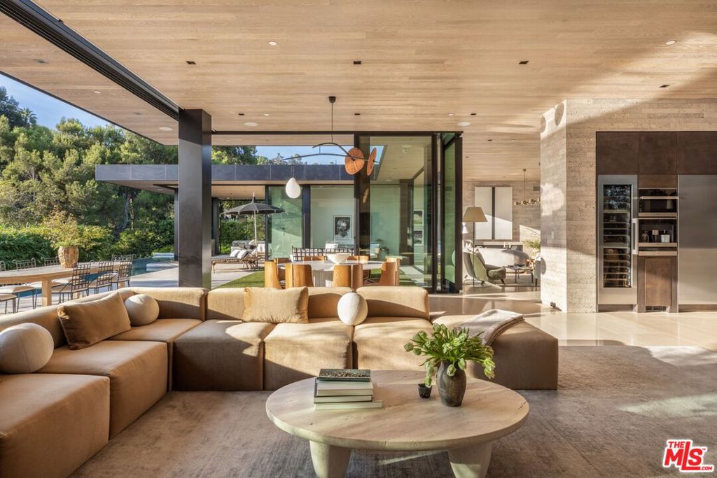 Discover world-class design and luxury in this organic contemporary Trousdale masterpiece crafted by award-winning architect Paul McClean and designer Lindsay Chambers and reimagined by Nate Berkus & Jeremiah Brent. Set on a prestigious, quiet cul-de-sac, this 11,000 SF home boasts an architectural exterior with custom Italian stonework. Mid-century-inspired steel grillwork surround the front door that opens to a showstopping glass bridge entrance. The two-story courtyard and walls of glass allow sunlight to fill the home and highlight the beautiful oak ceilings and Travertine walls. Glass walls open to a spectacular outdoor space featuring an expansive infinity pool with city and ocean views and a tranquil Japanese garden. The primary suite sits beside the pool as if it's floating above the water and offers a custom walk-in closet, and spa-like bathroom. Rejuvenate in the marble-clad indoor wellness center with hot and cold plunge, cedar sauna, and gym. Additional amenities include a stunning Nero Marquina-clad bar, home theater, subterranean auto gallery, and fairytale pink playroom. This architecturally significant home is a rare offering, even among the most discerning tastemakers in the city.