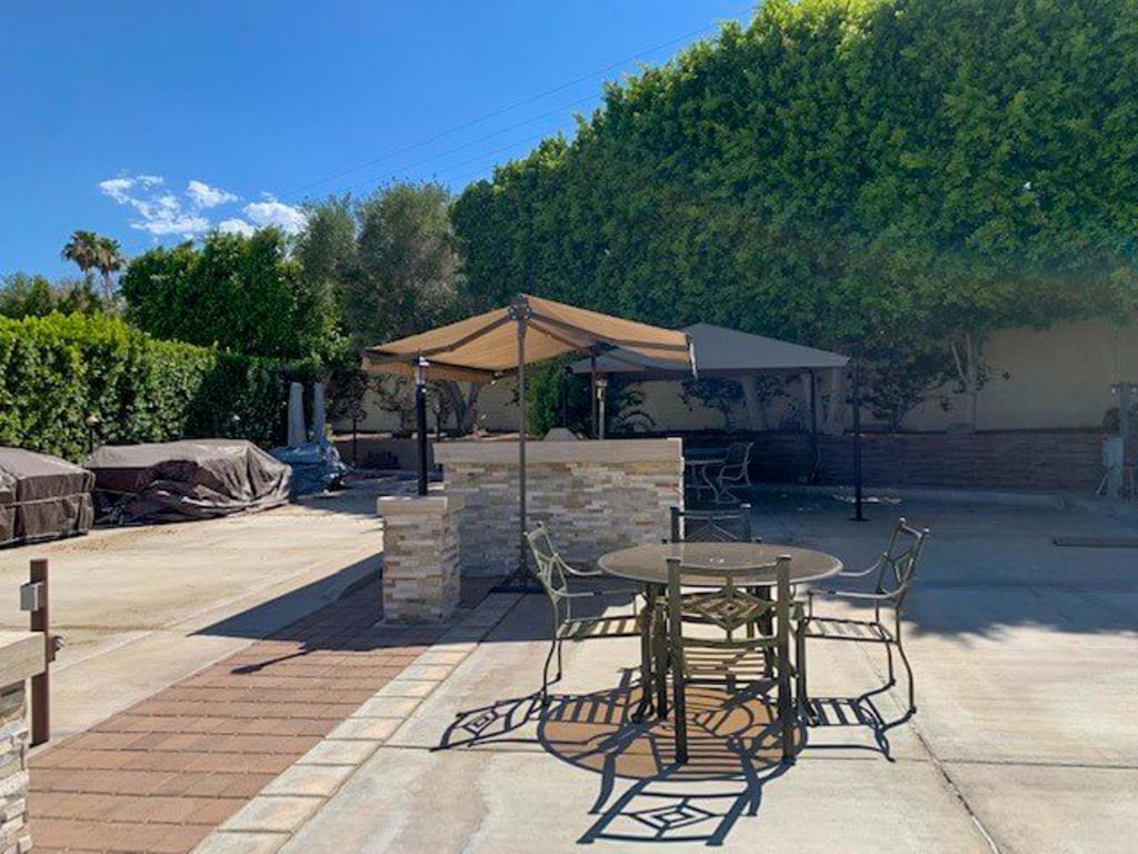 Peacefully situated along the perimeter wall, this east-facing luxury RV lot offers a serene retreat enhanced by a charming fountain, creating a welcoming ambiance for you and your guests. The lot features two matching wall post-lighting structures with convenient ledges, beautifully illuminating the space and adding functionality. With ample room for a 45-foot coach, a car, and a golf cart, the lot is designed for both comfort and convenience, offering the perfect mix of morning sun and afternoon shade. The recently added brick and paver back wall enhances privacy and provides a stylish touch, while the proximity to the perimeter pool, laundry, and showers adds to its appeal.The outdoor space is perfect for entertaining, featuring a remodeled L-shaped kitchen with tiled countertops, a double stainless steel sink with a faucet and garbage disposal, a two-burner propane cooktop, a built-in fridge/freezer, and a large stainless steel BBQ. The lot boasts two shade structures, including a spacious 1313 ft. area with lighting and a fan (needs new roof), and a roll-out sunshade over the kitchen, ensuring year-round comfort. Additional amenities include two storage containers, a stainless steel locking toolbox, and extra electrical outlets for added functionality. Surrounded by landscaping and offering both privacy and convenience, this lot is the perfect blend of style and practicality, ideal for those seeking the ultimate luxury RV lifestyle.‍‍