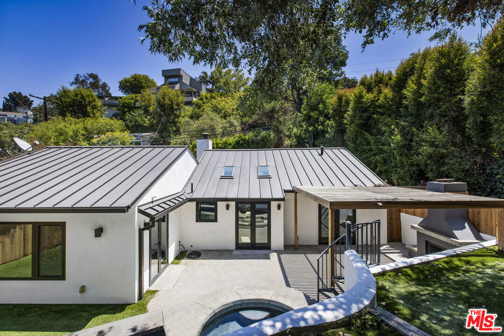 Tucked away in the coveted Hollywood Dell, this 1950s contemporary has been completely re-imagined as a private modern retreat. Freshly painted inside and out, the home is wrapped in verdant greenery and curated outdoor spaces, offering both serenity and style in the heart of the Hollywood Hills. An inviting front patio welcomes you into a sun-drenched open floor plan with vaulted ceilings, skylights, custom built-ins, and a fireplace at the heart of the living room - creating a warm and welcoming focal point. The spacious living area flows effortlessly into a chef's kitchen, complete with Wolf range, custom cabinetry, and quartz waterfall countertops, perfect for both quiet mornings and lively dinner parties. French doors open to a dreamy backyard escape complete with a heated swimmer's pool and spa, a pergola-covered dining area with fireplace, and multiple spots to lounge or entertain under the stars. Two bedrooms sit on one side of the home, flanking a beautifully appointed guest bath, while the oversized primary suite occupies the opposite wing. Vaulted ceilings, a spa-inspired bath with soaking tub and steam shower, and a generous walk-in closet complete this tranquil retreat. Additional upgrades include custom windows, a Sonos sound system, and a LifeSource whole-house water purification system - making this home as functional as it is beautiful.