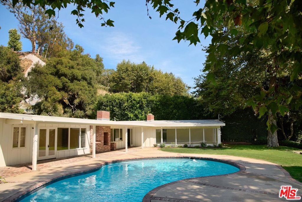 Privately tucked behind mature trees and lush landscaping, this soulful, single-story mid-century offers a rare blend of privacy, space, and natural beauty in one of Rustic Canyon's most coveted settings. Surrounded by mature landscaping and a gently flowing creek and set on an expansive 56,000-square-foot lot, the nearly 3,000 square foot 4 bedroom 4 bathroom residence lives in harmony with nature, with floor-to-ceiling windows framing serene canyon views, filling the interiors with light. Recently renovated, the home features brand new floors, updated bathrooms, a reimagined kitchen with an AGA stove, new appliances, a bonus gym/studio, and sauna. Clean architectural lines and organic materials create a timeless connection to the outdoors on the oversized lot, with multiple areas to enjoy: a large sparkling pool anchors the upper yard, while a footbridge over the creek leads to a spacious flat lawn ideal for entertaining or play. Tucked away on a private road just minutes from Rustic Canyon Park, this is one of the most picturesque and private properties on the westside. Offered fully furnished with designer pieces or also available unfurnished.