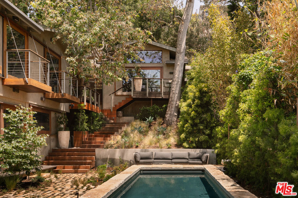 This Santa Monica Canyon refuge invokes a sense of nostalgia and harmony with nature in its purest, undiluted form; a masterful transformation by LA's very own David Hertz FAIA, the widely acclaimed pioneer in sustainability and the use of recycled building materials. The famed architect was tasked with the creation of a 'contemporary tree-house' oasis, and the Venice/Malibu native delivered. Hidden beneath a canopy of trees that shroud the property from the street, this masterwork portfolio case study is adorned with sustainably harvested tropical hardwoods and emphasizes natural ventilation principles for an energy-efficient build. Natural sunlight slowly moves across interior surfaces, welcomed inside by oversize clerestory and picture windows, skylights, and pocket doors to maximize an easy indoor-outdoor lifestyle. Custom wood details can be found in every room, from vaulted mahogany ceilings in the living room to the cabinets and open shelving of the custom Poliform kitchen. Even the staircase to the second level is a statement piece, itself a fusion of more than 600 individual planks resulting in a striking visual display. The primary wing is designed to inspire calm, rest, and rejuvenation with its warm woods, smooth stones, and panes of glass. The luxe organic bathroom has two stone-basin vanities separated by a double rainwater shower, French doors to the outside, and pedestal soaking tub and continues to an open custom wardrobe. Radiant heating has been installed in the primary bath, kitchen, and office, and the guest house includes one bedroom and one bathroom. Relish cool ocean breezes from numerous sundecks, balconies, terraces, and eco-conscious gardens. Relax in the shimmering pool and spa or entertain, barbecue, and dine al-fresco from within this private, magical paradise secluded from the outside world by mature sycamores, Ipe walls, and bamboo. Truly a one-of-a-kind offering and a rarity in the marketplace, there is nothing comparable to this special home in the area. Welcome to a fresh, mindful lifestyle in one of the most coveted, ideal sections of Santa Monica, close to beaches, parks, canyon trails, and the numerous fine dining and shopping options of the Westside.