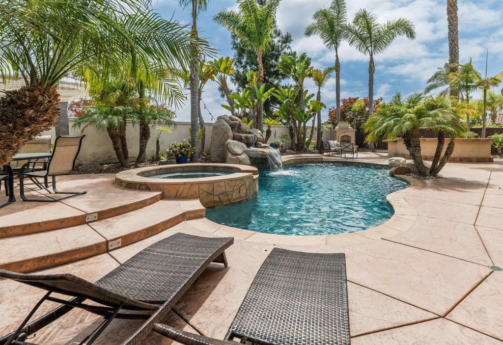 Located on a quiet cul-de-sac in the highly sought-after Viadana community, this expansive Carlsbad home pairs laid-back luxury with everyday comfort—offering over 3,300 square feet of thoughtfully designed living space. The flexible floor plan is ideal for modern living, with a main-level guest suite and adjacent bath, a private home office with French doors and a walk-in closet, and seamless indoor-outdoor flow that makes entertaining feel effortless. Just minutes from top-rated Carlsbad schools, scenic trails, and North County’s most loved beaches and golf courses, this home offers a lifestyle that feels both convenient and effortlessly relaxed. A gated front courtyard creates an inviting first impression, opening to a bright and airy interior finished in a soft neutral palette. Sunlight pours through oversized windows, accentuating the upgraded tile flooring and plush new carpet. The formal living room welcomes you with two walls of windows, while the adjacent dining room impresses with soaring ceilings and a dramatic rotunda layout that brings architectural interest and a sense of openness. Just across the hall, the home office offers flexibility—with French doors that open to the courtyard, the dining area, and the back hallway, it’s easy to imagine it as a creative studio, quiet retreat, or potential sixth bedroom. At the heart of the home, the open-concept kitchen and family room are made for connection. Granite counters, a built-in fridge, gas range, double ovens, and an oversized island provide space to prep and gather, while the generous cabinetry space keeps everything organized behind the scenes. Large windows overlook the backyard and create a natural connection between the interior and your own private outdoor retreat. Upstairs, the rotunda landing leads to a serene primary suite with a spacious ensuite bath, complete with dual sinks, a makeup vanity, soaking tub, walk-in shower, and a large walk-in closet. Two additional bedrooms share a full bath with dual sinks, and a nearby laundry room with sink and linen storage keeps things practical. A spacious loft opens to a breezy balcony, while an adjoining bonus room—complete with wet bar and built-ins—makes the perfect media room, home gym, or flex space for your evolving needs. Step outside and you’re instantly transported. A sparkling saltwater pool with a large tropical waterfall, a relaxing spa, and lush landscaping framed by mature palms create a resort-like vibe. The built-in outdoor kitchen with bar seating makes entertaining a breeze, while multiple seating areas invite you to unwind. Additional upgrades include fully owned solar (installed 2023), air conditioning, EV charger, whole house fan, smart security system with Ring doorbell, and automated irrigation and lighting. There’s even a first-floor storage closet to keep everything out of sight but within easy reach. All this just minutes from top-rated Aviara Oaks Elementary and Middle Schools, the Batiquitos Lagoon trails, Dove Library, local shops and restaurants, and some of North County’s most iconic beaches and golf courses. Whether you’re starting your day with a quiet coffee in the courtyard or ending it with a dip in the pool, this home invites you to slow down and enjoy the best of coastal California living.