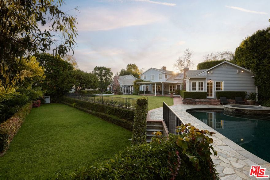 Celebrity compound on 1 acre south of Sunset - private, gated, and expansive. Beyond double gates and twenty-foot hedges, 196 Granville Avenue reveals a rare Brentwood estate with an unmistakable sense of history and presence within the neighborhood. A sweeping semi-circular driveway introduces the Cape Codinspired home, where dappled sunlight filters through mature trees and the facade recalls the elegance of a Hamptons summer home, reimagined for Southern California living. Inside, the chandelier-lit foyer opens to formal living and dining rooms designed for entertaining, complemented by original hardwood floors and light-filled spaces that flow effortlessly between one another. The kitchen, envisioned for daily gathering, showcases a central island, open shelving, and a breakfast banquette overlooking the gardens. Adjacent, the family room captures the home's character and warmth with vaulted wood-beamed ceilings, a stone fireplace, and French doors that open to the backyard. The main-level primary suite includes its own fireplace, dual-entry walk-in closet, and a serene bath with soaking tub, shower, and direct access to the pool. A secondary en-suite completes the first floor, while the upper level offers two additional bedrooms and a shared bath. Above the three-car garage, a private space with its own ensuite and walk-in closet provides endless possibilities for a gym, home office, or maid's quarters. Outdoors, the property unfolds like a hidden resort across a series of terraces and gardens that feel almost otherworldly in their privacy. Stone walkways meander through lawns and vine-draped verandas, leading to a pool and spa framed by mature trees. A lower path descends to a secluded lawn secondary flat yard for a sport court or pavilion. Further along, trails weave through the estate's own park-like terrain, leading to a grotto bar beneath a waterfall and a creek bordered by redwoods. A two-bedroom, two-bath guesthouse completes the estate, offering a full kitchen, living and dining areas, ideal for multi-generational living or an income opportunity, with a private entrance for independence. Held by one of television's most beloved figure for nearly thirty years, 196 Granville Avenue represents a piece of Hollywood history and a once-in-a-generation development opportunity to own one of Brentwood's most private, character-rich compounds south of Sunset.