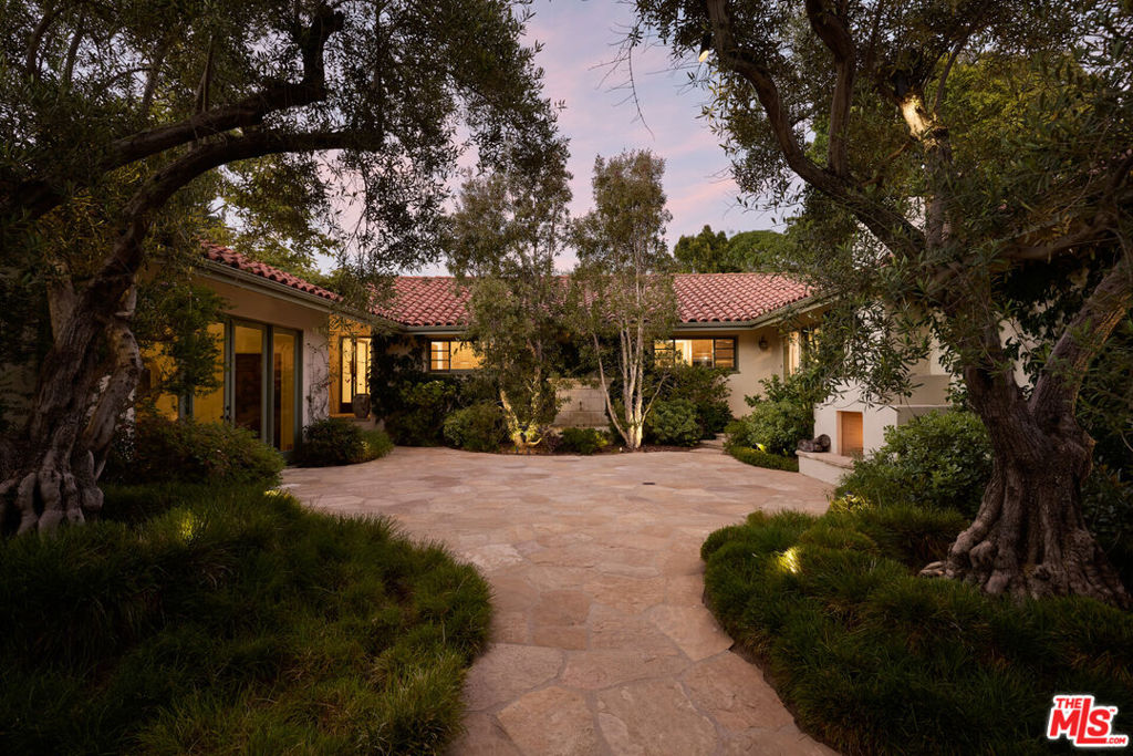 Set on a half-acre lot just moments from the Riviera Country Club, 1296 Capri Drive is a single-story estate that fuses European provenance with a thoughtful, full-scale renovation rooted in craftsmanship, indoor-outdoor flow, and connection to nature. A gated entry opens to a serene front courtyard with an outdoor fireplace, framed by mature plantings. An antique bronze and glass front door opens to expansive interiors where every room connects to the surrounding gardens. Throughout the home, old-world elements include 15th-century Italian doors from Milan, a carved Louis XV marble fireplace, and two antique French stone fountains that define the courtyard and anchor the backyard. The floor plan is organized into two distinct wings. One dedicated to the private living quarters, including the primary suite, which opens to the gardens and features dual bathrooms with a smart toilet, dry sauna, and two walk-in closets. Three additional en-suite bedrooms complete this side of the home. The opposite wing is designed for entertaining, centered around a den with a built-in bar, surround sound, antique terracotta flooring, and a climate-controlled wine wall. The main living room features a carved marble fireplace and vaulted, beamed ceilings that invite natural light throughout the day. A full wall of French doors opens to the gardens, reinforcing the seamless indoor-outdoor connection that defines the property. The kitchen was custom built by Cooper Pacific, centered around Italian feather walnut travertine counters and professional appliances that include a 64-inch Wolf range with French top and grill, two Wolf ovens (one steam), Le Cornue rotisserie, Sub-Zero refrigeration, dual Miele dishwashers, Wolf refrigerator drawers and ice maker, Irinox flash freezer and sous vide, and a built-in Natufia hydroponic grower. A walk-in pantry and separate china closet offer ample utility without compromising design. Outdoors, the landscaping is as functional as it is peaceful. Created by Garett Carlson of Landarc and Stephen Block of Inner Gardens, the grounds include a series of vegetable garden beds with lemon, orange, peach, plum, fig, mulberry, yuzu, Australian finger lime, and avocado trees. The soil and all plantings were organically treated. Additional highlights include a 2,500 bottle refrigerated wine cellar, rose-covered gazebo, built-in outdoor speakers, multiple 100-year-old Olive trees, and an area ideal for a dog run. The home features two new HVAC systems with HEPA filtration, all-new attic ducting and insulation, three water heaters (two of which are tankless), and security cameras.
