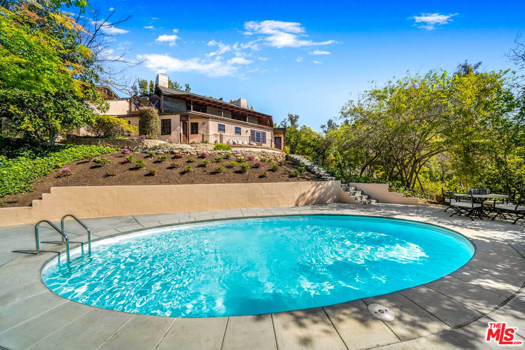 This one-of-a-kind character home featured in multiple media outlets such as Robb Report and Dwell was the estate and workspace of the late celebrity and iconic fashion photographer Melvin Sokolsky for almost 50 years. Originally built in 1939 and designed by architect Frederic Barienbrock for a silent screen actress, the rich history and creative spirit of this inspiring property is a piece of Beverly Hills' cultural legacy. Perched on a knoll at the end of a secluded cul-de-sac and surrounded by nature in the foothills of Benedict Canyon, the peaceful landscape features an English garden with heirloom roses against the backdrop of serene Century City vistas. Located just minutes from world class shopping and restaurants on Rodeo Drive, this hillside sanctuary offers an unparalleled living experience. A long, brick-paved, gated driveway leads to an enchanting 5 bedroom and 4 bath Country Colonial Revival residence with European interior design details that exudes warmth and sophistication. Upon entering the home, you are greeted by a dramatic foyer with Degas-inspired powder room. Highlights include beautiful custom wood built-ins, imported clay tile flooring throughout, two wood burning fireplaces, wood-paneled study and wood beamed ceilings. Adjacent to the formal dining room is a rustic farmhouse kitchen featuring artisanal wood counters, sitting island, commercial stainless steel glass door display refrigerator and professional chef's stove. Expansive lower primary suite offers an adjoining bathroom with separate dressing area. A spacious outdoor rear deck that wraps around the back of the house is the perfect place to lounge and gaze at the city lights. The property grounds of over 18,000sqft offer a remodeled pool with new hardscaping and landscaping to complete this unique property. Lot APN #4348018012 is included in sale. Not subject to ULA tax in the city of Beverly Hills.