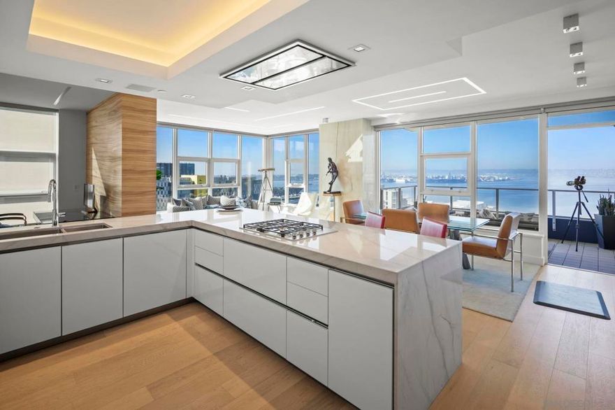 Truly one-of-a-kind, fully upgraded luxury residence in Bayside on Millionaire’s Row. This southwest-facing corner home offers sweeping bay, city, and sunset views and underwent a complete $500K+ down-to-the-studs remodel in 2018. Every detail was reimagined to enhance light, views, and craftsmanship, with meticulous care from the original owner. Enter through a dramatic foyer with coffered ceilings, designer lighting, custom Koa wood cabinetry imported from Hawaii, and built-in wine storage. The open-concept living, dining, and kitchen spaces showcase floor-to-ceiling views, Duchateau flooring, quartzite stone accents, sleek ceilings with modern lighting, and a private balcony ideal for relaxing or entertaining. The chef-inspired kitchen features custom German cabinetry, quartzite counters, Miele appliances, and breakfast seating. The serene primary suite includes its own balcony, custom Koa furnishings, a larger-than-original walk-in closet with California Closets, and a spa-style bath with dual sinks and walk-in shower. A flexible layout includes a home office plus guest room with custom Zoom bed and a designer bath with soaking tub. Additional upgrades include power blinds, built-ins throughout, and two premium side-by-side parking spaces with EV charger and storage located near the elevator. Bayside features a newly renovated lobby, 24-hour concierge, pool, spa, sauna, steam room, movie theater, wine lounge, conference room, BBQ areas, and library. Just steps to Little Italy, Waterfront Park, the Rady Shell, Petco Park, and San Diego’s best dining and entertainment!  Retreat to the serene primary suite with its own private balcony, custom Koa furnishings, and a larger than original walk-in closet with a California Closet system and custom built-ins. The spa-inspired bath offers dual sinks, a walk-in shower, and striking custom stonework. A flexible floor plan includes a home office and guest bedroom with a custom Zoom bed, while the guest bath offers a freestanding soaking tub and designer finishes. Additional highlights include power blinds throughout (blackout in bedrooms), ample storage, and two side-by-side premium parking spaces with a dedicated electric charger for your Tesla or other electric vehicle, conveniently located just outside the elevator with separate storage. Bayside residents enjoy a newly renovated lobby, 24-hour concierge, pool, spa, sauna, steam room, movie theater, conference room, wine lounge with oversized chiller, BBQ areas, library, and more. Perfectly located, you’re steps from Little Italy, the Gaslamp, Waterfront Park, Petco Park, the Rady Shell, and San Diego’s best dining, shopping, and entertainment. This residence represents the very best in luxury downtown living on the front row to the waterfront.