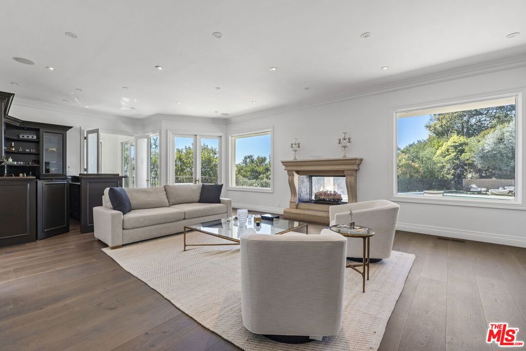 Welcome to this stunning 5-bedroom, 6-bath Mid-Century home located in Beverly Hills' coveted Trousdale Estates. Set on nearly half an acre of flat land, this home epitomizes the quintessential Trousdale layout, with expansive walls of glass offering unobstructed views of the oversized pool and sparkling canyon lights. As you pull up the long driveway, you'll feel as though you've entered a world far from the hustle of LA. Upon entering the foyer, you're immediately drawn into the grand living room, which features a statement fireplace, a sunken bar, and an adjacent formal dining room. The doors open seamlessly to the expansive outdoor patio, which boasts various seating areas, an outdoor dining area, and a cozy fireplace perfect for entertaining or relaxing. The large pool is ideal for a leisurely afternoon dip or a few laps, while beyond the pool, the spacious backyard invites you to sit back, relax, and take in the serene surroundings. The master suite anchors the home, offering a walk-in closet and a luxurious en-suite bathroom with a soaking tub. Three additional bedrooms and a large bonus room complete the sleeping quarters, with the bonus room perfect for a home gym or a play area for the kids. The kitchen is a chef's dream, featuring a beautiful island in the center and high-end appliances that are perfect for hosting and entertaining guests. Initially built in 1969, this home has been meticulously renovated, offering a perfect blend of timeless design and modern amenities. It's versatile layout makes it the ideal home for a wide range of tenants. The house is located in the Beverly Hills school district. The house is available furnished or unfurnished. An additional cost will apply if tenants choose to lease the home with furniture.
