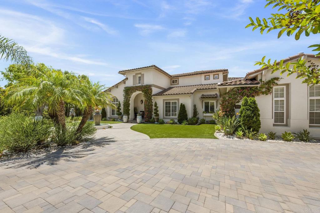 Nestled in the highly coveted gated community of Savenna in 4S Ranch, this stunning 5-bedroom, 5.5-bathroom home offers 5,128 sq. ft. of luxurious living space. A dramatic two-story foyer welcomes you with jaw-dropping views out of the back as far as the eye can see. The sunken formal dining room features coffered ceilings, while the living room is accented by rich wood flooring, built-in cabinetry, and large windows that flood the home with natural light. The chef’s kitchen is both stylish and functional, featuring white cabinetry, granite countertops, a walk-in pantry, and high-end appliances, including a 6-burner gas range. It opens seamlessly to the family room, which includes a built-in wet bar, wine fridge, fireplace, custom built-ins, and expansive windows that capture peaceful views of the surrounding hills—perfect for both everyday living and entertaining. A full bedroom and en-suite bathroom on the main level provides ideal accommodations for guests or multi-generational living. Two dedicated office spaces and a flexible bonus room—perfect as a playroom, den, or media room—add even more versatility. Upstairs, the spacious primary suite is a true retreat with a fireplace, private covered balcony, dual walk-in closets, and a luxurious ensuite with soaking tub, separate shower, dual vanities, two toilets, and a private bonus room ideal as a gym or office with its own balcony. Three additional upstairs bedrooms each have their own en-suite bathrooms, offering privacy and convenience for family or guests. Step outside to your private backyard oasis with no neighbors behind and unobstructed views of rolling hills. The property backs up to hundreds of acres of beautiful, preserved land, creating a sense of openness and tranquility. Enjoy a saltwater pebble-tec pool with endless current system, built-in BBQ with bar seating, a large turf lawn, multiple lounge areas, and a pergola with TV and fountains—an entertainer’s dream. Additional highlights include a 4-car garage with epoxy flooring, owned solar, a Tesla charging unit, 2 Tesla Powerwalls, a brand-new tankless water heater, whole-house water filtration and leak detection systems, and a downstairs laundry room with built-ins and a sink. Thoughtful design elements such as custom millwork, cabinetry, and interior doors elevate the home’s craftsmanship throughout. Located in a quiet, rarely available enclave of 4S Ranch, this home offers the perfect blend of privacy, space, and sophistication in an exceptional setting.