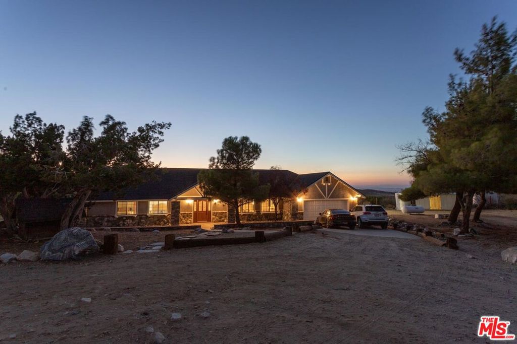 Nestled amidst the captivating High Desert Hills, just adjacent to the Angeles National Forest and a renowned national park, lies this approximately 2.5-acre equestrian property at 29243 Piani Road in Pearblossom. This modern ranch home offers over 2,000 square feet of living space, designed to capture breathtaking sunsets from the elevated position of the back of the house that faces west, showcasing a serene retreat in a stunning setting. The home encompasses three bedrooms, a versatile office/flex room, and two bathrooms, each with double sinks and bathtubs. Designed for comfort and practicality, it features vaulted ceilings and an array of custom finishes, including brick and wood floors in the kitchen and dining room, complemented by Turkish Travertine in the Venetian Pattern in other living areas. Large windows fill the space with natural light and showcase the picturesque views. A separate outside entrance to the primary bedroom and the dining room, as well as a utility room entrance, underscores the thoughtful design of this home. The 2-car attached garage provides ample storage space, with additional storage available in the attic and a large utility room pantry. Say goodbye to high electricity and water bills, as this home is powered by a high-quality paid-off solar system with 26 panels installed by Solar Optimum in 2022, and water sourced from its own well and propane for gas. In addition to central heating, this home is equipped with a whole-house evaporative cooler, a highly energy-efficient alternative to traditional air conditioning. The dining room also features a wood-burning stove for cozy winter evenings. The private, fully fenced lot, with its 330-foot frontage on Piani Road, is complemented by a grand wooden ranch gate, creating an impressive entrance to this serene retreat. With RV hookups and ample outdoor storage, this property accommodates a variety of needs, whether for ranch living or leisure. Equestrian facilities abound, with a 120' x 80' arena, a 50' round-pen, and a spacious hay barn capable of accommodating a full semi-truck load. The property supports multiple horse stalls with water and electricity, ensuring your equine companions enjoy optimal care. There is also a Nelson Automatic waterer in the pasture area. Beyond its equestrian amenities, the property is steeped in nature, providing direct access to miles of trails and seasonal creeks. It is conveniently located approximately five miles from local amenities, including the USPS, LA County Fire Department, and Pearblossom Park. Embrace the opportunity to own this equestrian property, where natural beauty, modern comforts, and horse-friendly facilities converge. Whether you are an avid equestrian or seeking a tranquil retreat, this home offers a unique chance to live in a truly stunning setting.