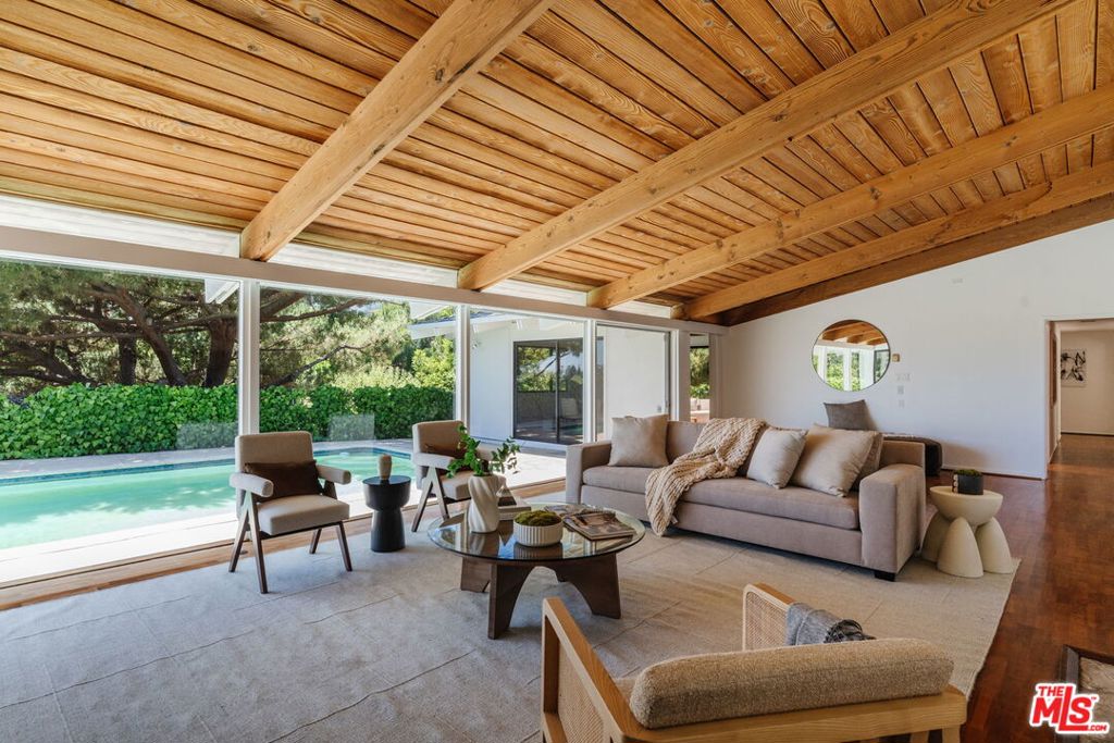 Nestled at the end of a long, private drive in the coveted Kenter Canyon enclave, 508 Tuallitan Road is a sprawling single-level retreat that celebrates classic Mid-Century architecture, tranquil natural surroundings, and seamless indoor-outdoor living. Enter to discover soaring vaulted ceilings with exposed wood beams, a striking stone fireplace, and expansive floor-to-ceiling glass doors that frame verdant views while inviting in soft, dappled light. The open-concept living spaces flow effortlessly into the outdoors, where a sparkling pool and multiple wraparound patios offer idyllic venues for lounging, entertaining, or dining al fresco. The formal dining room stuns with architectural detail -- an intricate, wood-beamed ceiling and generous volume -- flanked by patio access for the ultimate in California-style entertaining. The adjacent kitchen is sunlit and functional, ideally positioned to serve gatherings with ease. Three spacious bedroom suites, each with vaulted ceilings and peaceful garden outlooks, offer the utmost in comfort and privacy. The primary suite features its own covered patio for morning coffee or evening reflection, creating a true sanctuary. A cozy den is an ideal office or homework hub, while a dedicated laundry room enhances day-to-day functionality. Thoughtful storage is integrated throughout, from abundant interior closets to an exterior shed with a built-in workbench -- great for creative pursuits or weekend projects. Located moments from Brentwood's premier schools, boutiques, and dining destinations, yet supremely tucked away in a quiet canyon setting, this peaceful retreat is a rare fusion of architectural authenticity, timeless design, and livable luxury in one of the Westside's most sought-after neighborhoods.