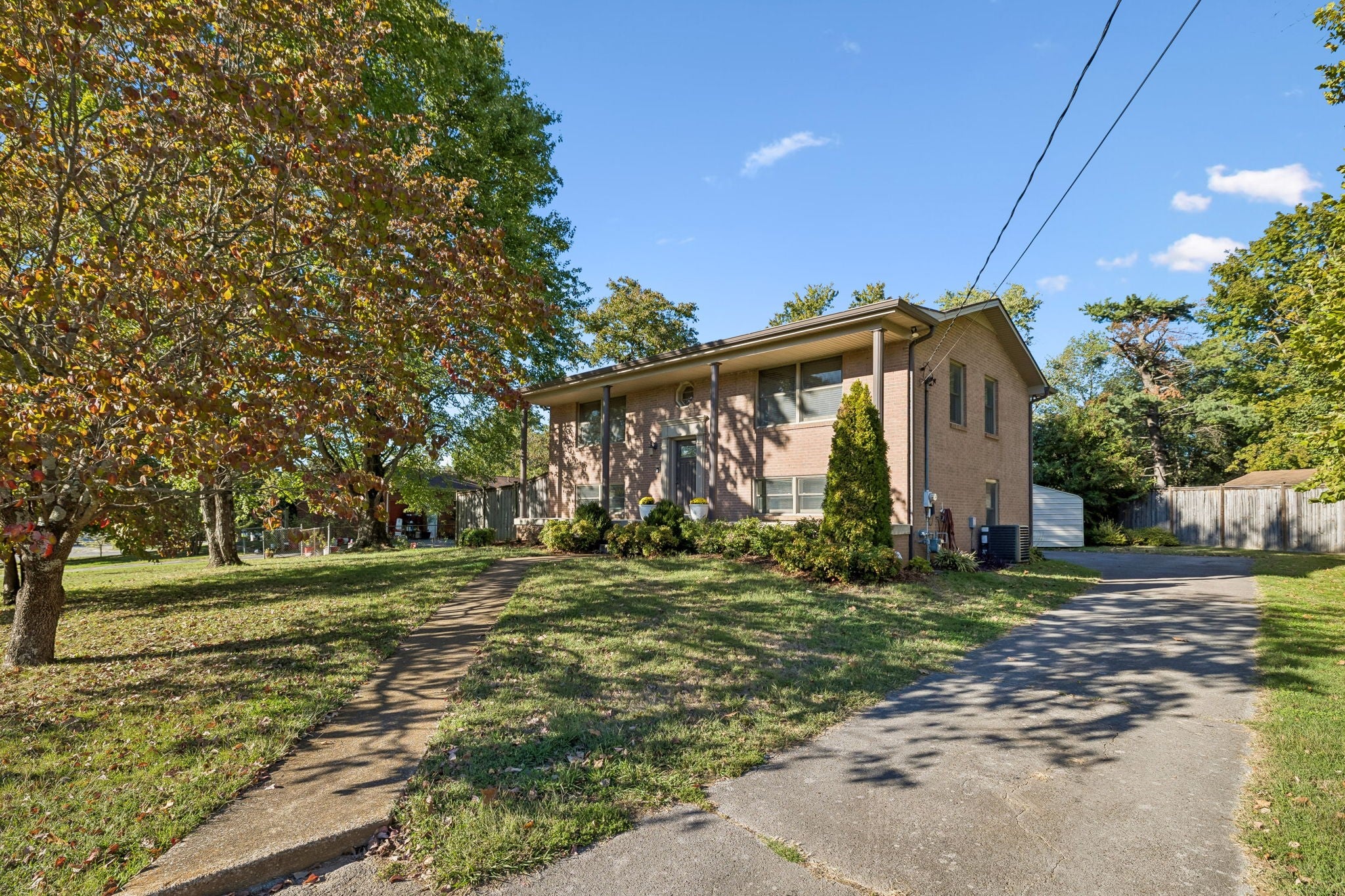 3-bed home for sale in Hermitage, TN 37076, 203 Tyler Dr Side view of a tan brick two-story house with a paved driveway, a small detached shed and mature trees along the lot