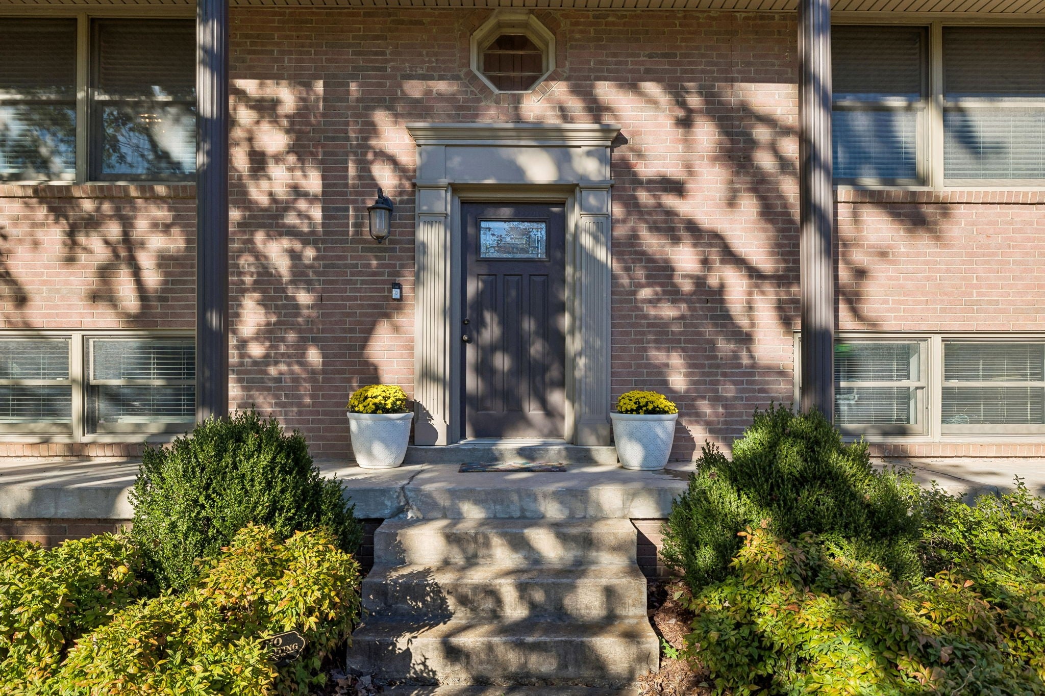3-bed home for sale in Hermitage, TN 37076, 203 Tyler Dr Entry door framed by stone steps, brick walls, round window above the door and potted plants beside the landing