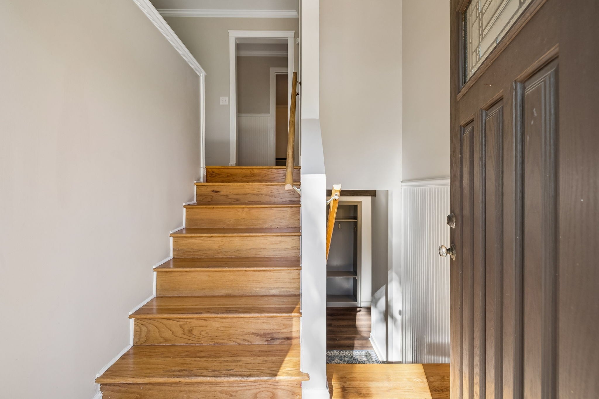 3-bed home for sale in Hermitage, TN 37076, 203 Tyler Dr Staircase with wood treads and a wood handrail beside a dark entry door, with a closet opening at the base