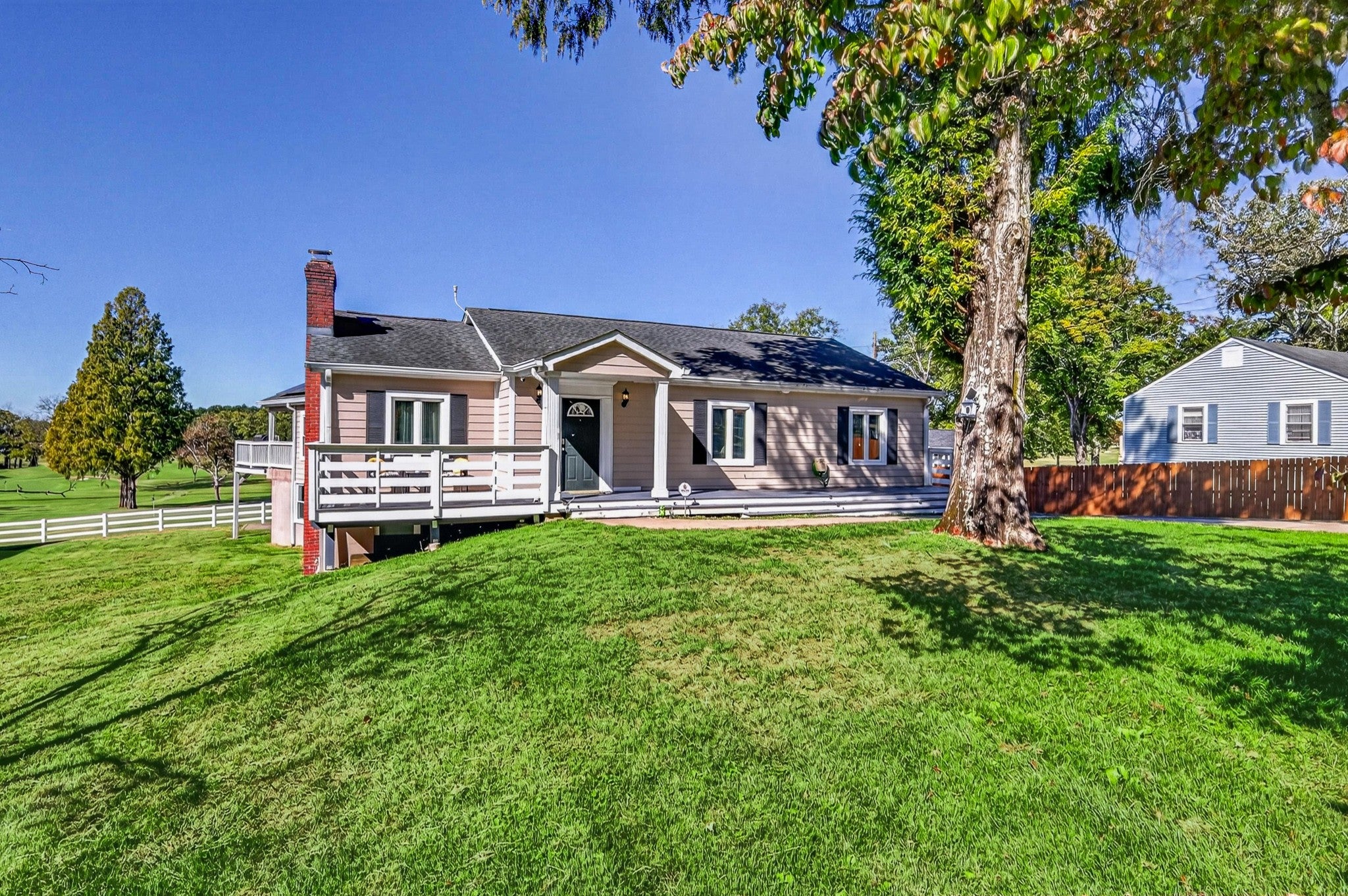 6-bed home for sale in Old Hickory, TN 37138, 130 Park Cir Single-story tan home with a brick chimney and a front deck, with a wooden fence and trees beyond the lawn
