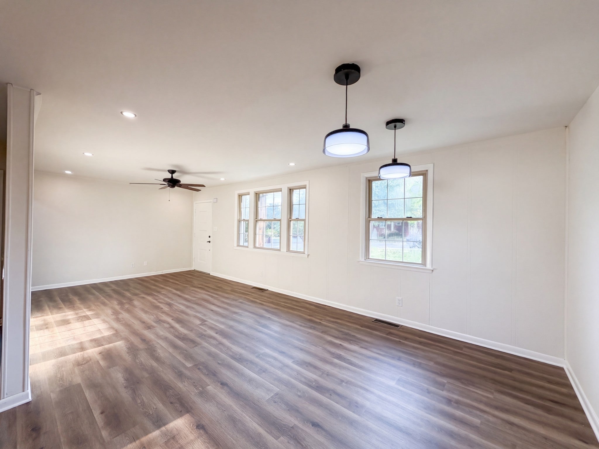 Open living room with wood-look vinyl flooring, pendant lights over a row of windows and a ceiling fan