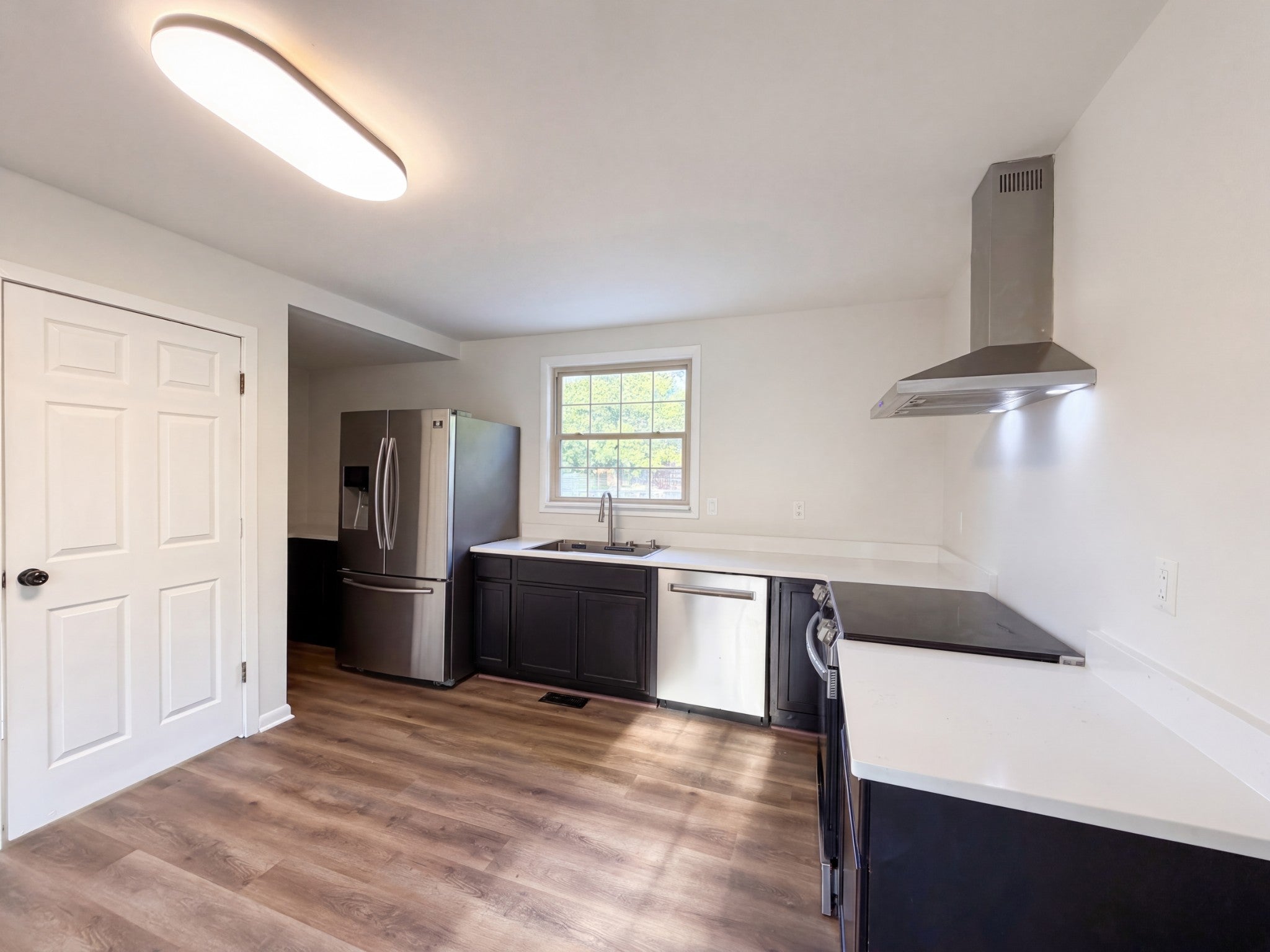 Kitchen with dark lower cabinets, a stone countertop, stainless steel range hood and a window over the sink