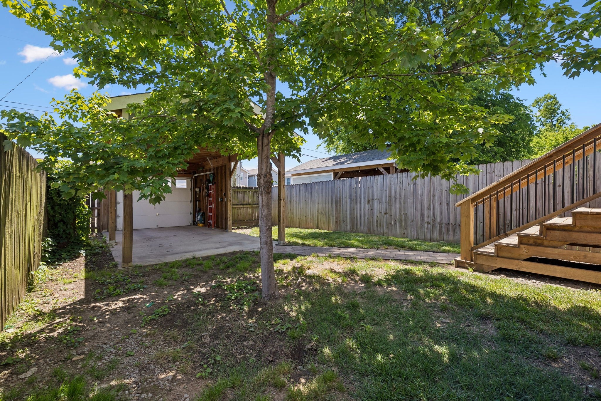 3-bed condo for sale in Nashville, TN 37209, 6205a New York Ave Back yard with a shade tree, grass, a paver walkway, a covered carport and a wood privacy fence, with wood deck stairs at right