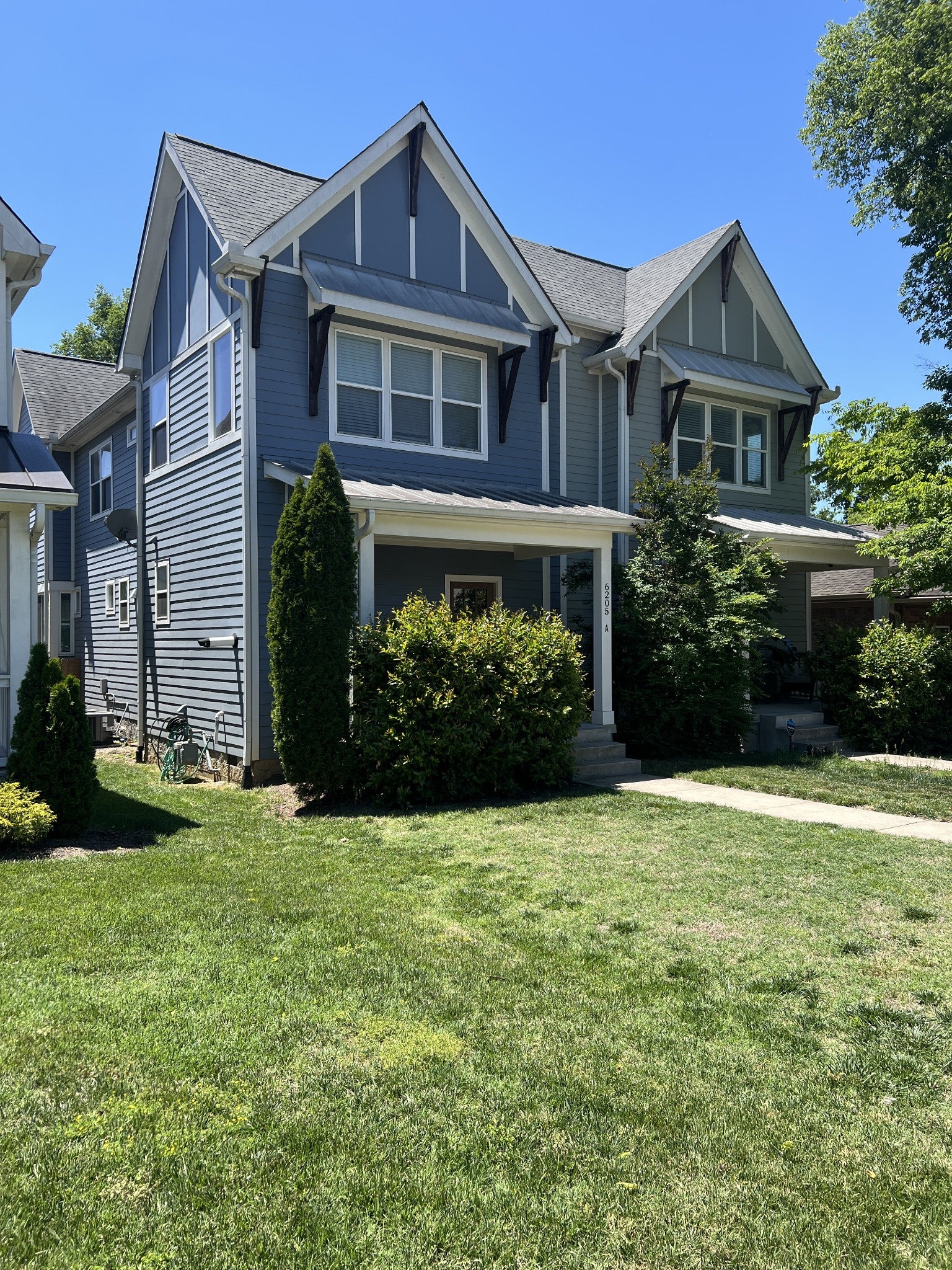 3-bed condo for sale in Nashville, TN 37209, 6205a New York Ave Side view of a two-story blue townhouse with a covered front porch, dark decorative brackets and a grassy front yard