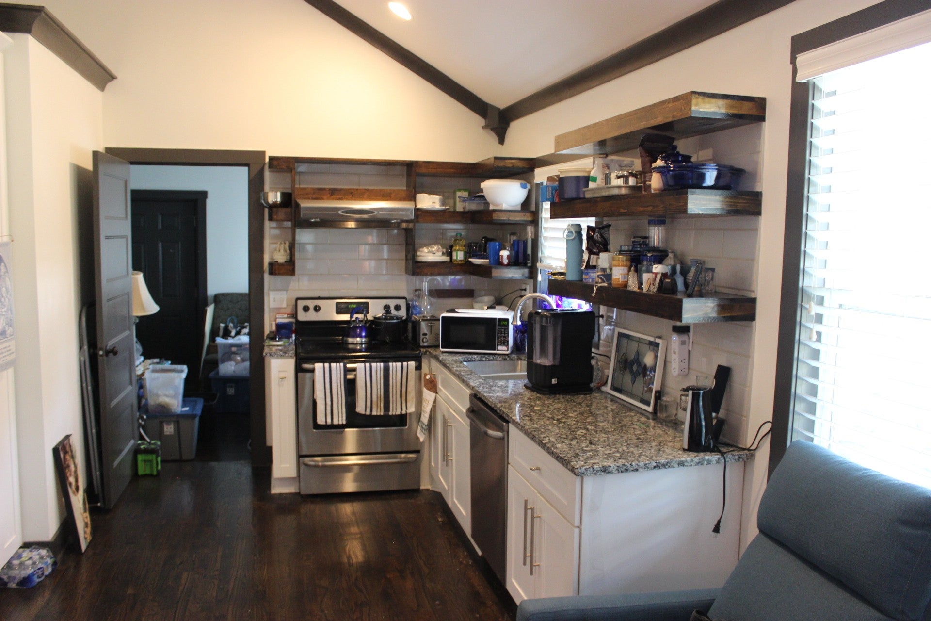 Kitchen with a vaulted ceiling, open wood shelves, white cabinets and stone countertops beside a window