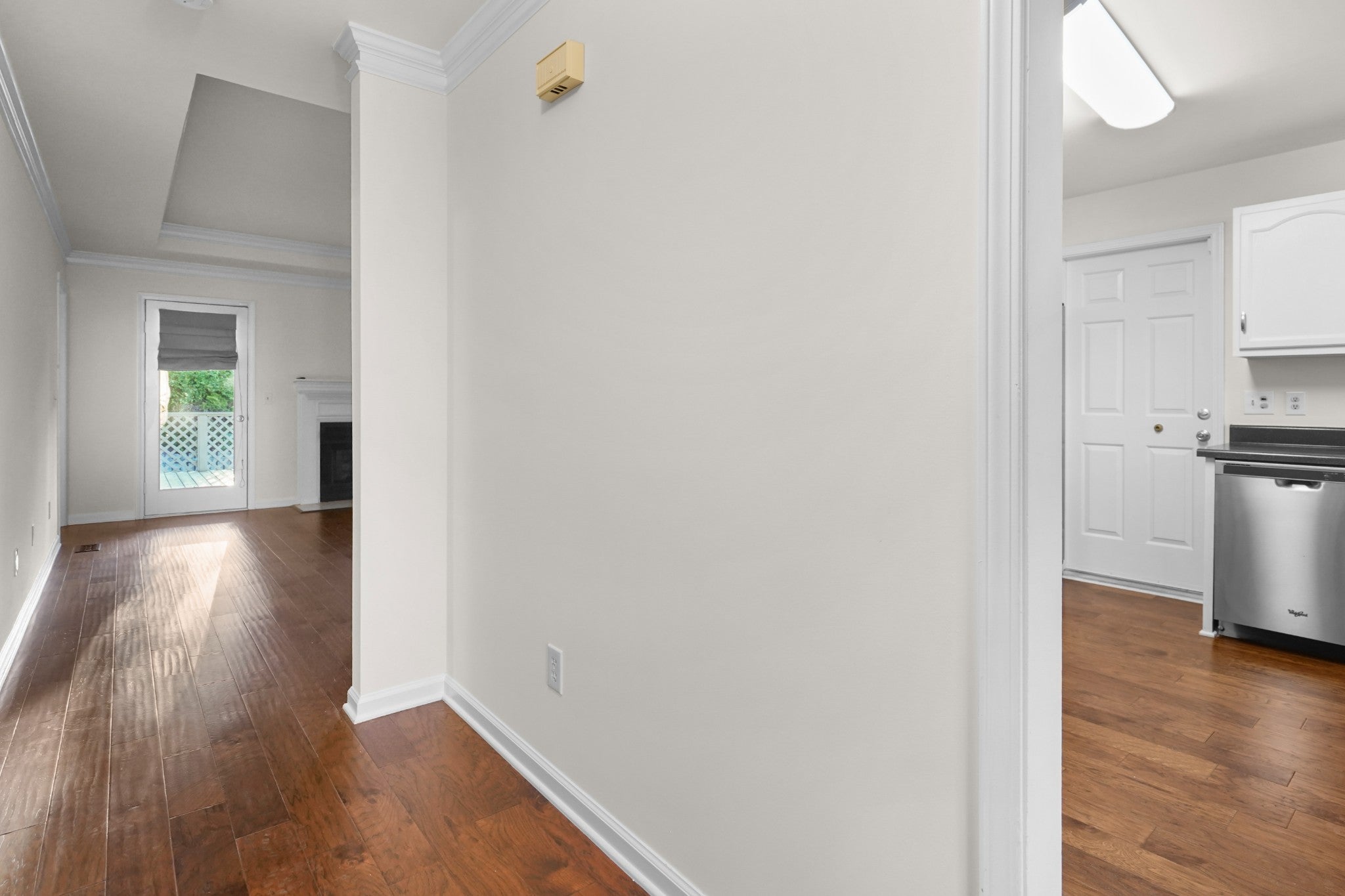 Hallway with wood floors and crown molding leading to a room with a fireplace and a glass door to the back deck
