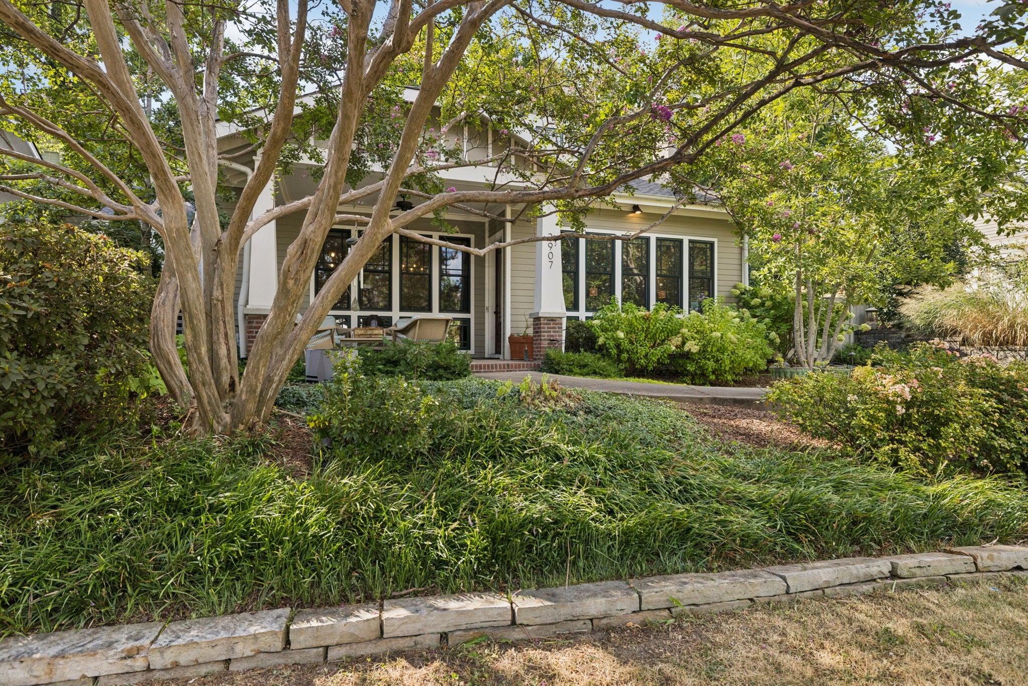 Front of the house with a covered porch, stone edging along the lawn and a row of tall windows under the roofline