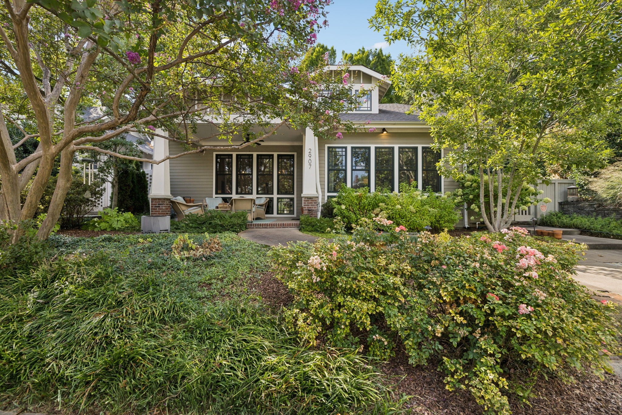 Covered front porch with multiple tall windows, brick porch columns and shrubs lining the walkway
