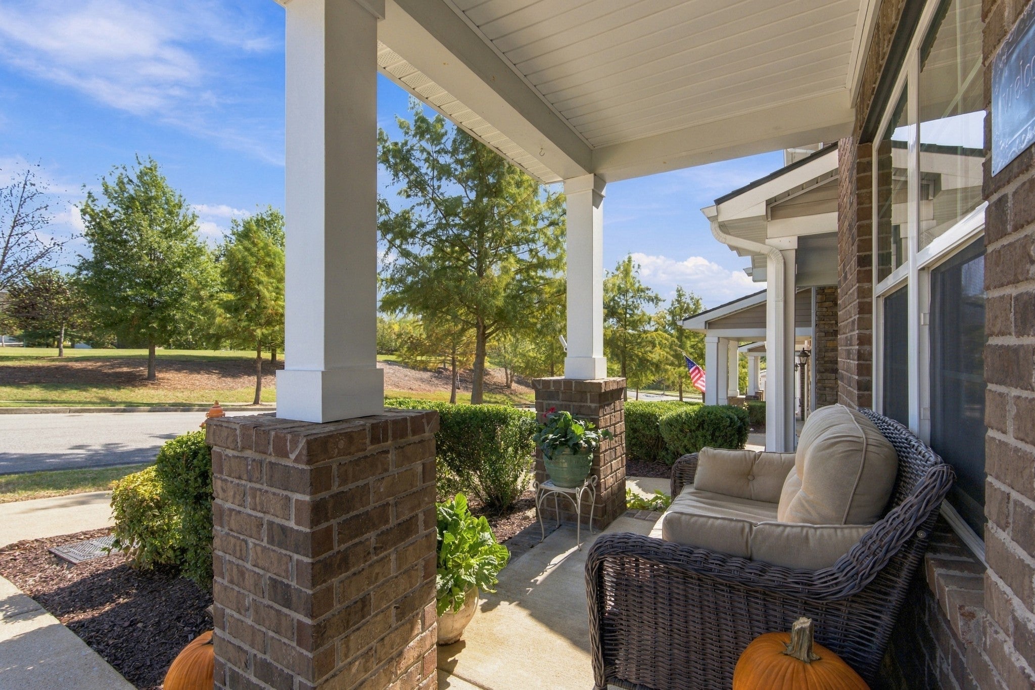 Covered front porch with white square columns, brick piers and a wicker settee beside a window