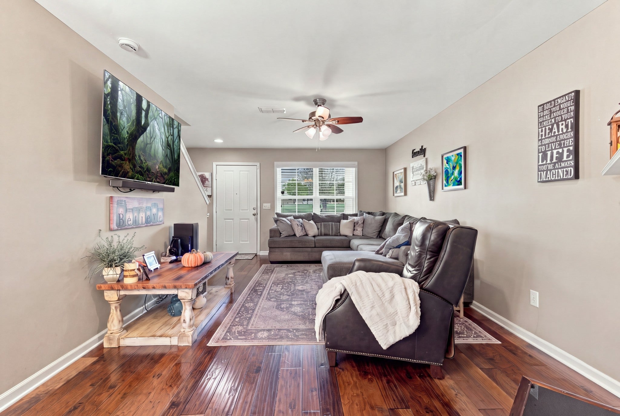 Living room with wood-look floors, a sectional sofa, a ceiling fan and a wall-mounted television