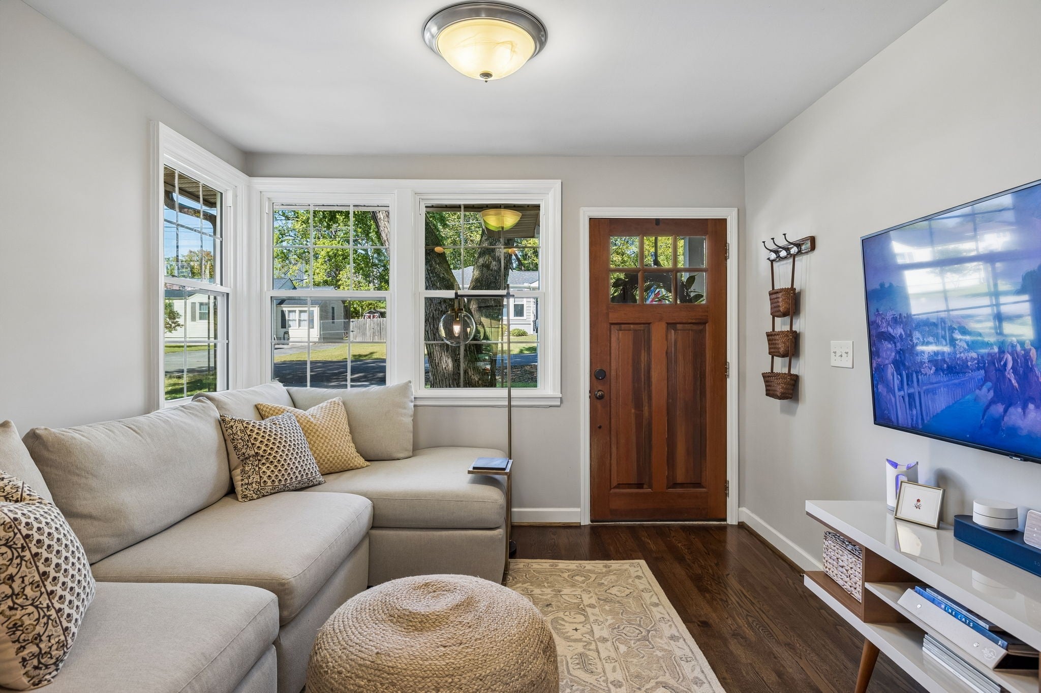 Living room seating area with a sectional sofa, a bay window overlooking the street and a rug over wood floors