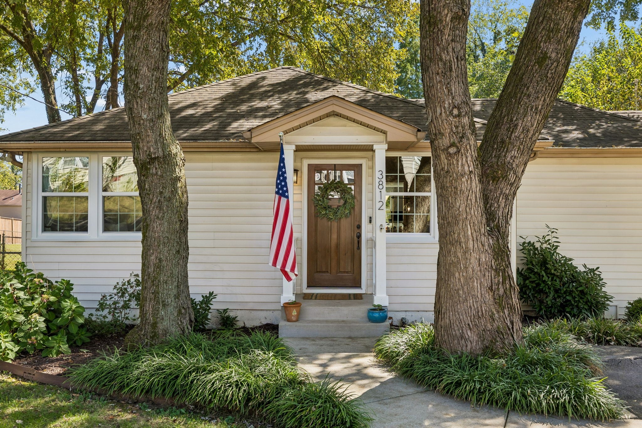 Front entry with a dark wood door, white columns and a small gabled overhang, flanked by windows and low shrubs