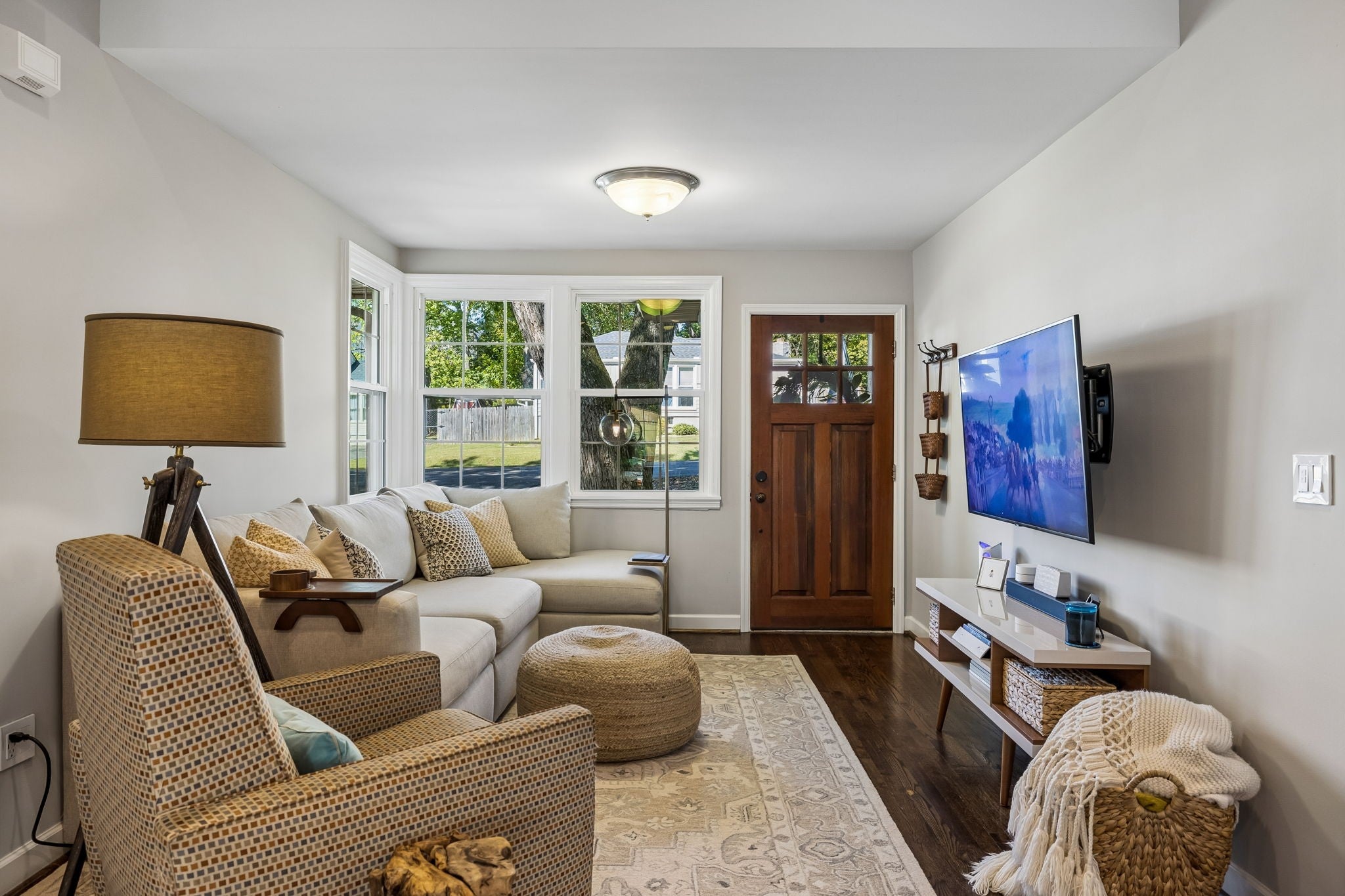 Living room with a wood-look floor, a light sectional sofa, a bay of windows and a wall-mounted television