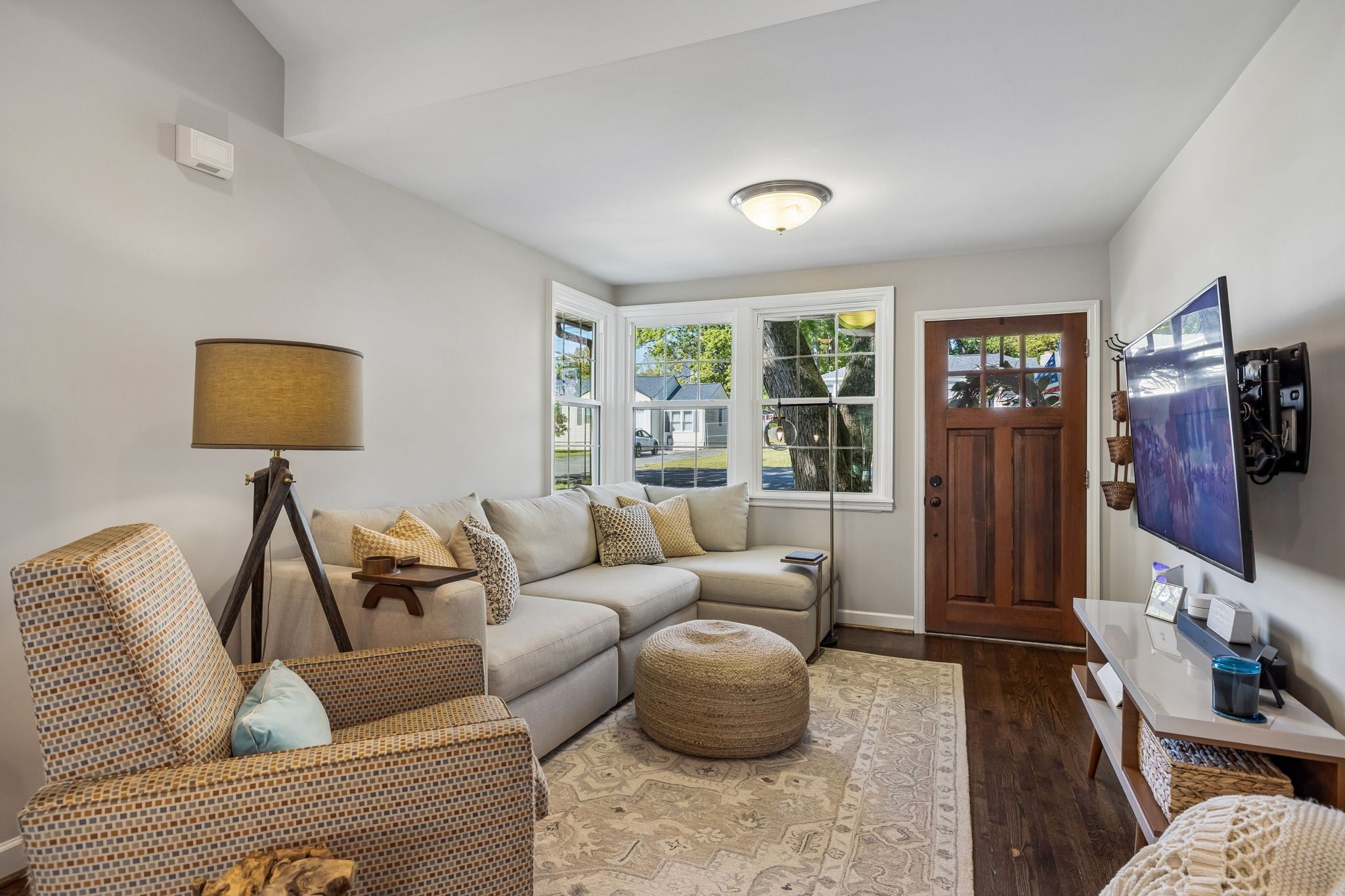 Living room from another angle showing the front door, a bay window and a wall-mounted television on a low media stand